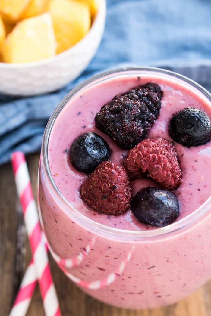 This Mango Berry Smoothie combines fresh mango with mixed berries into a refreshing smoothie recipe. This fruit smoothie is perfect for breakfast or a snack! overhead photo of a glass of Mango-Berry Smoothie topped with fresh berries