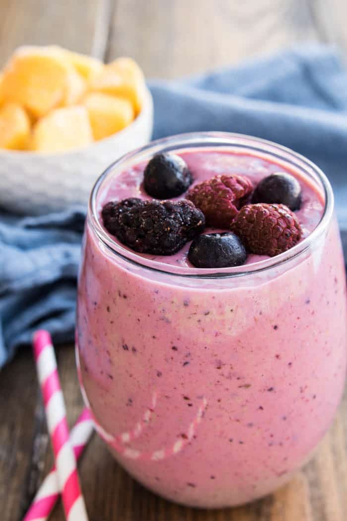 This Mango Berry Smoothie combines fresh mango with mixed berries into a refreshing smoothie recipe. This fruit smoothie is perfect for breakfast or a snack! A glass filled with a Mango-Berry Smoothie and fresh berries on top