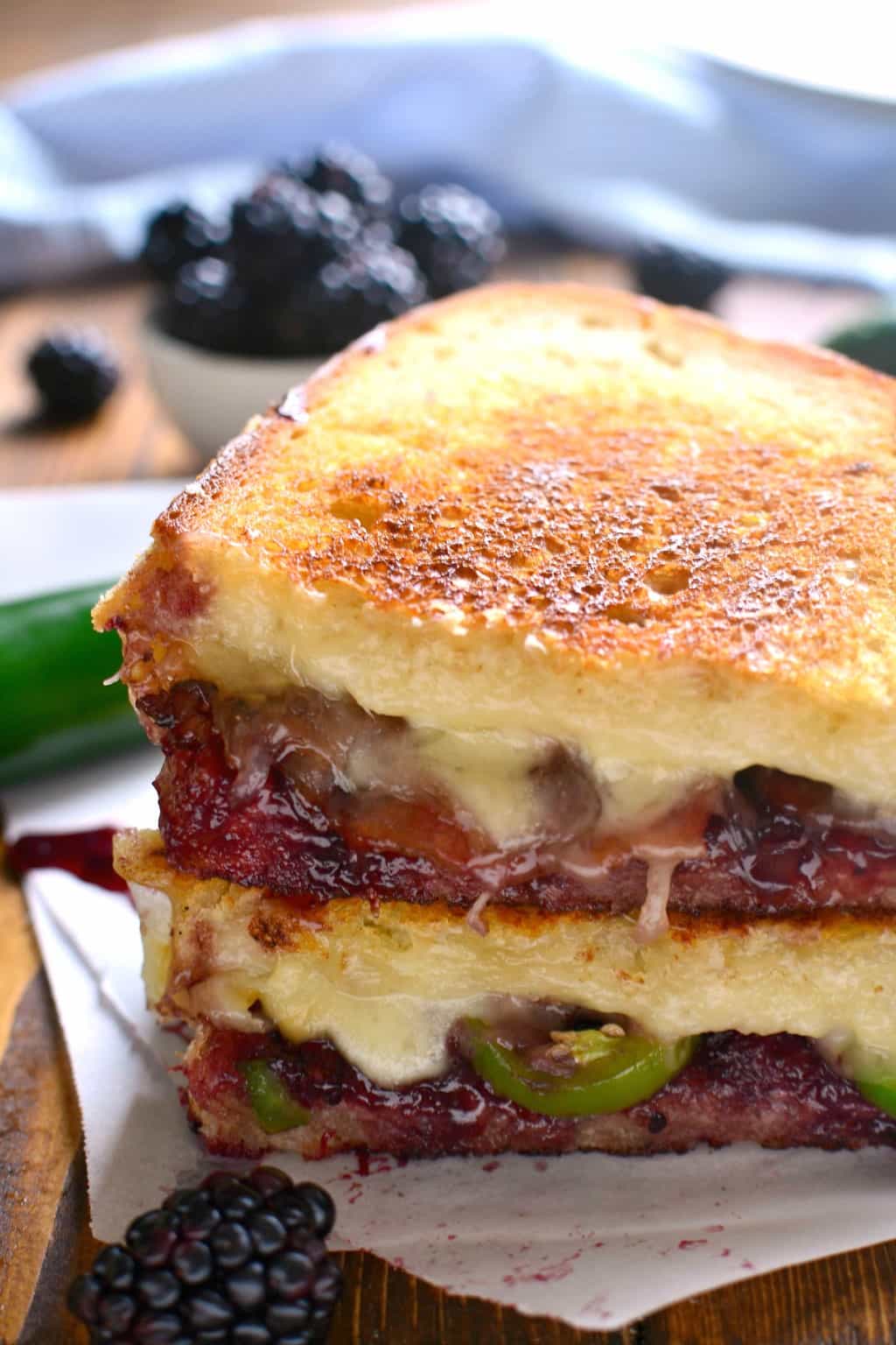 Blackberry Bacon Grilled Cheese is the perfect combination of savory and sweet! Made with Swiss cheese, blackberry jam, fresh jalapeños, and crispy bacon, it's a must try for ALL sandwich lovers! grilled cheese sandwich on white bread made with swiss cheese, blackberry jam, jalapenos and bacon