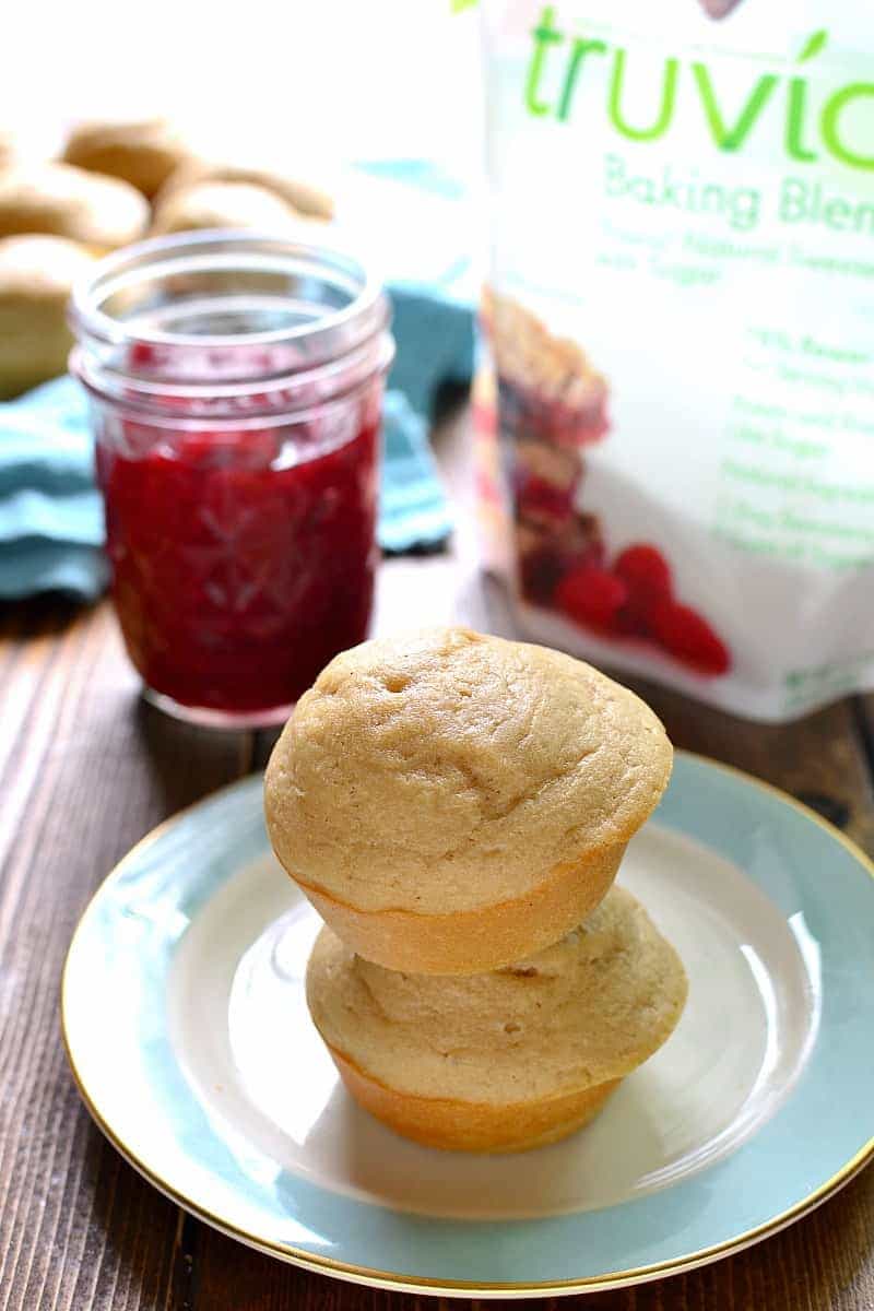 2 vanilla muffins stacked on a plate next to a jar of homemade jam