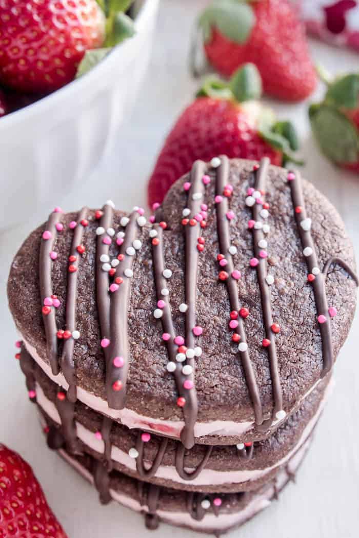 Chocolate Strawberry Sandwich Cookies...just in time for Valentine's Day! You're sure to fall in love with these adorable heart-shaped cookies - perfect for classroom parties, teacher gifts, or a special Valentine's Day treat. A delicious combination of chocolate sugar cookies and strawberry cream filling, they're surprisingly easy to make and seriously fun to eat. And with a little drizzle of chocolate and some fun colored sprinkles on top, they're exactly what you need to make this Valentine's Day extra special!