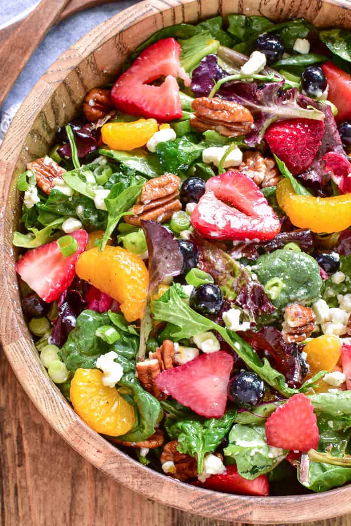 Variety of summer salads on a table, including summer pasta salad, summer fruit salad, and a leafy green summer salad with fresh strawberries.