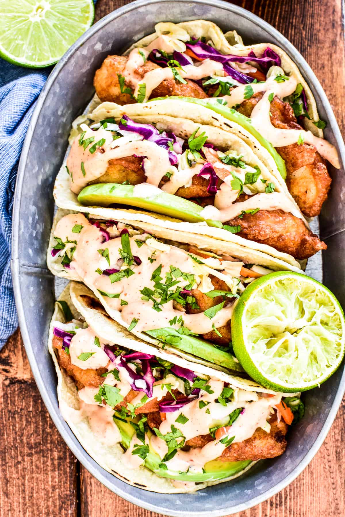 Overhead shot of Baja Fish Tacos in a serving tin with avocado, fresh cilantro, and chipotle mayo