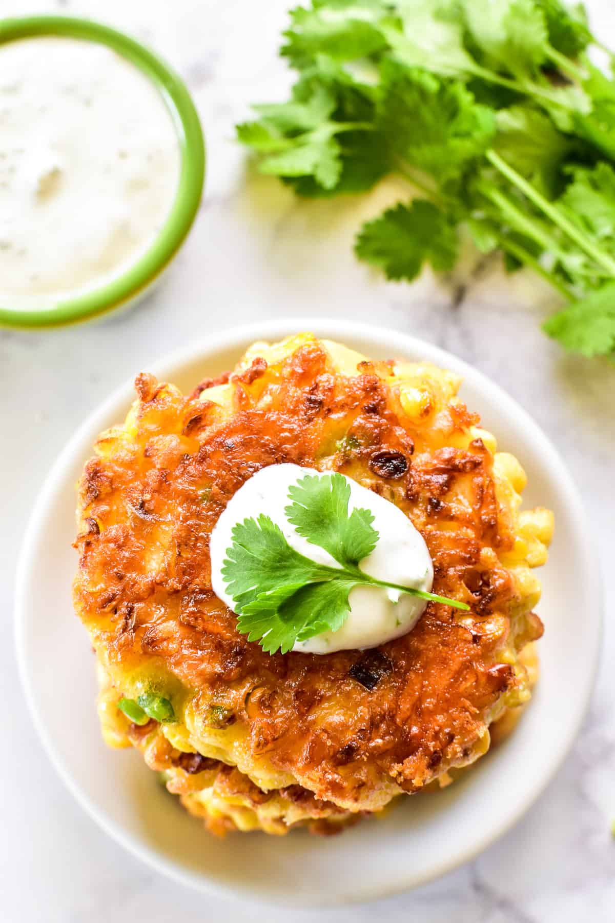 Overhead shot of Corn Fritters on a small white plate with creamy cilantro sauce and fresh cilantro