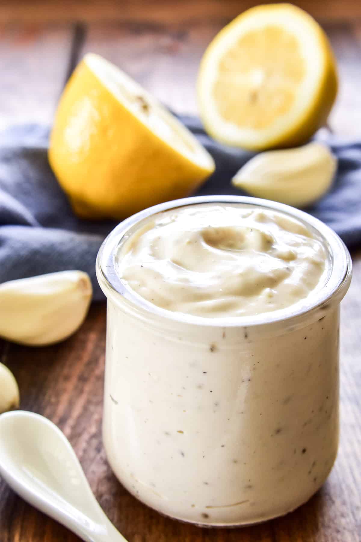 Garlic Aioli in a small glass jar with fresh garlic and lemons in the background