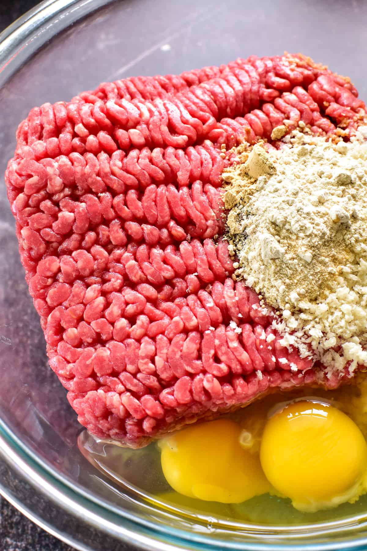 Close up of ground beef, eggs, breadcrumbs and seasonings in mixing bowl