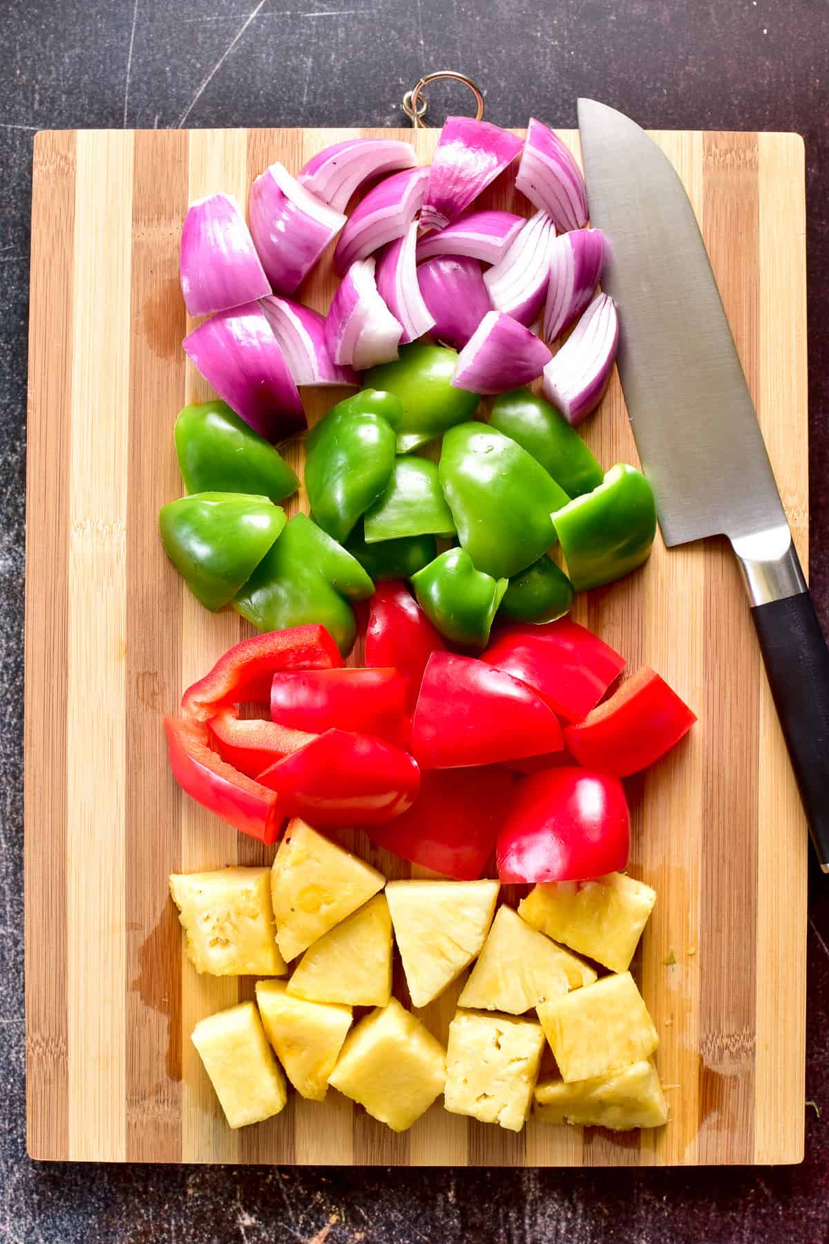 Overhead shot of peppers, onions, and pineapple chopped on a cutting board