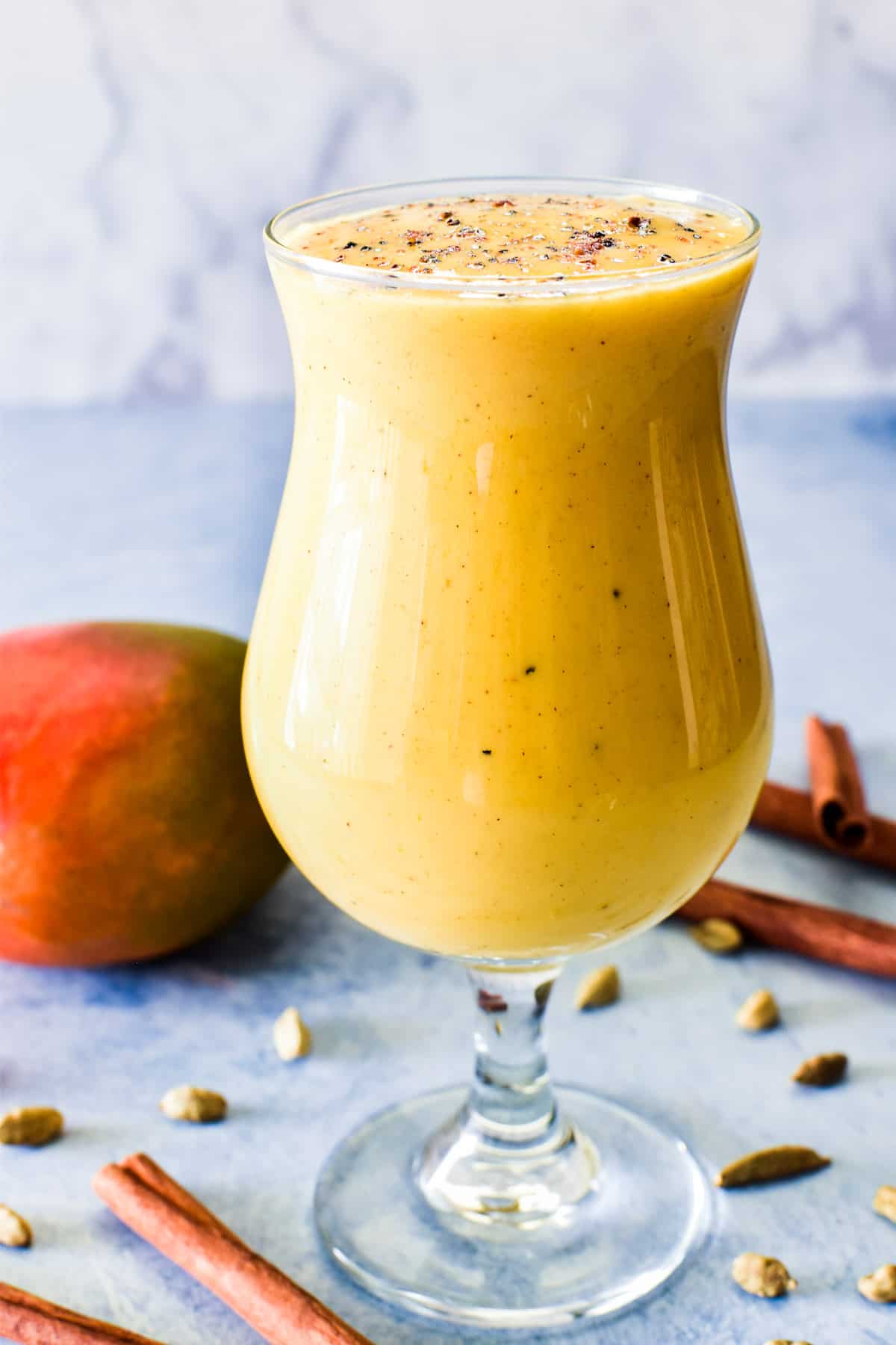 Mango Lassi in a glass with cardamom pods and cinnamon sticks