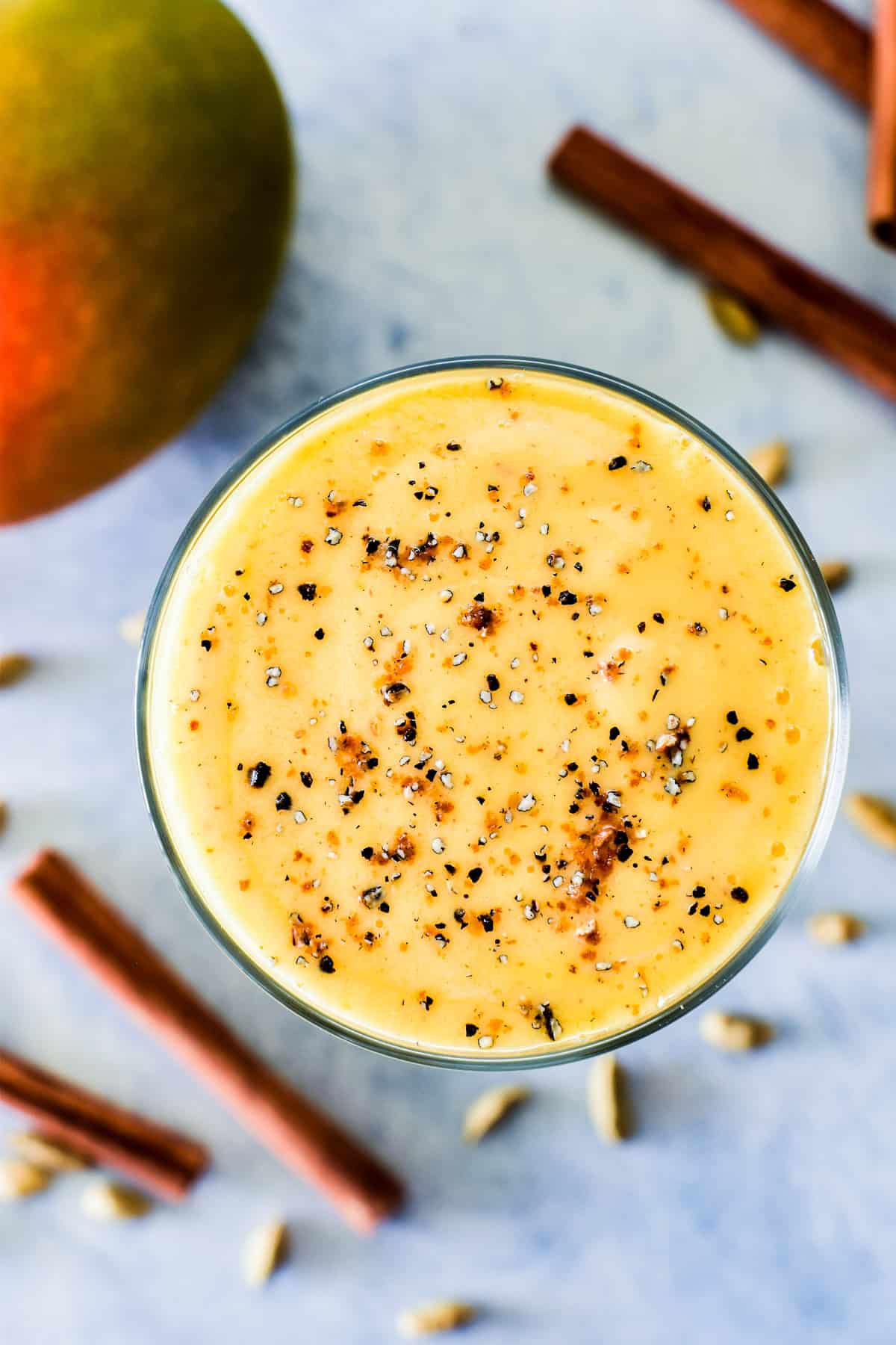 Overhead shot of Mango Lassi in glass garnished with cardamom and cinnamon