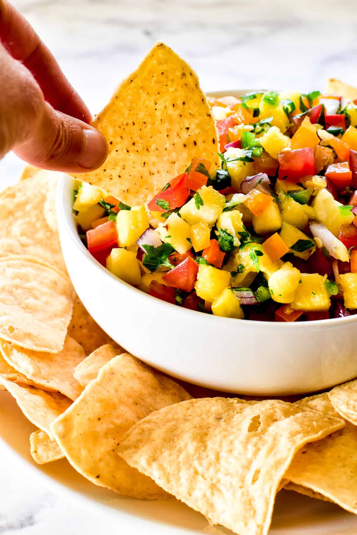 Close up of tortilla chip being dipped into pineapple salsa