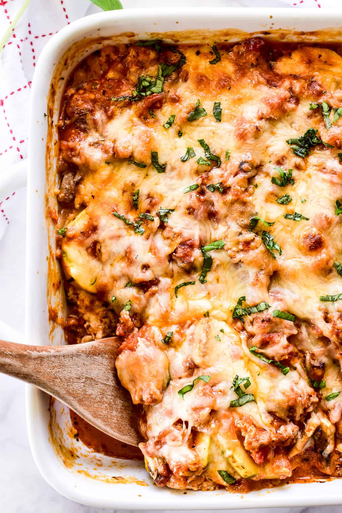 Overhead shot of Zucchini Lasagna in white pan with wooden serving spoon