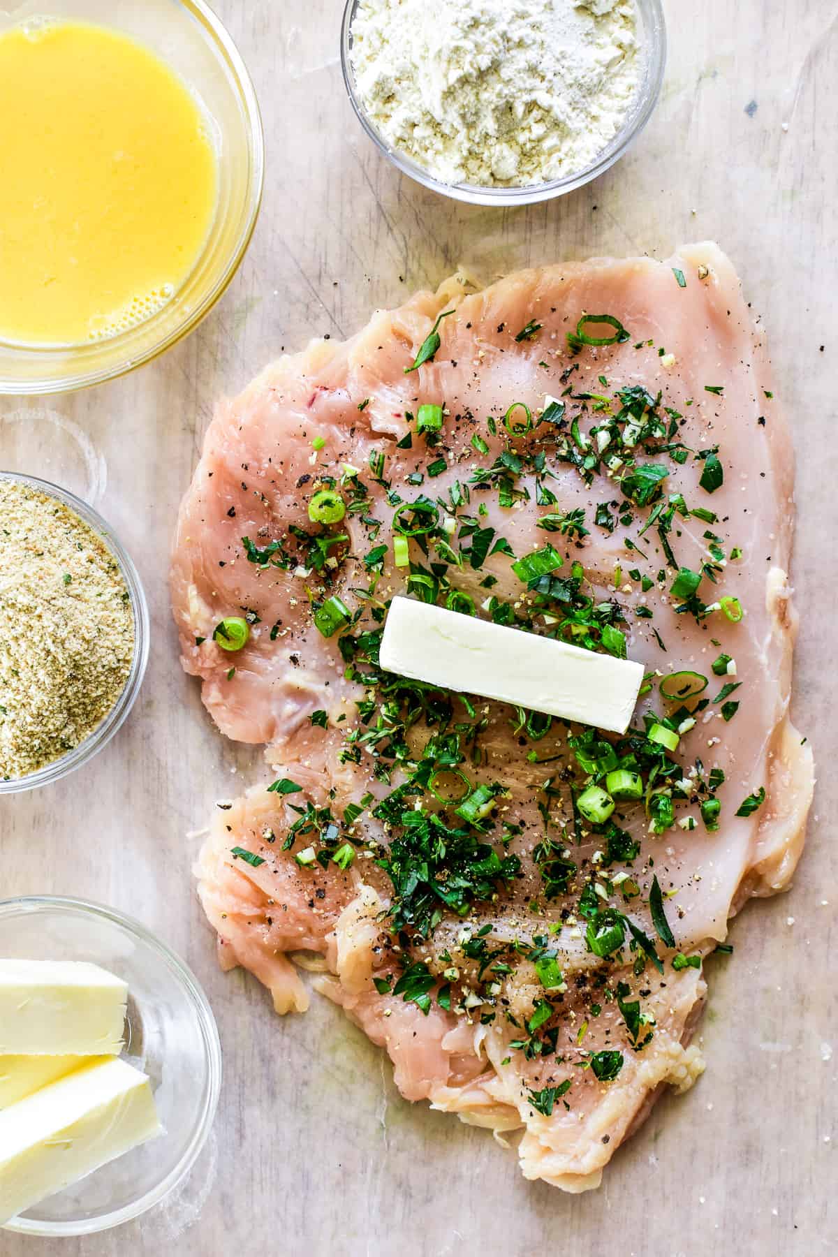 Overhead prep shot of flattened chicken breast with butter and herbs