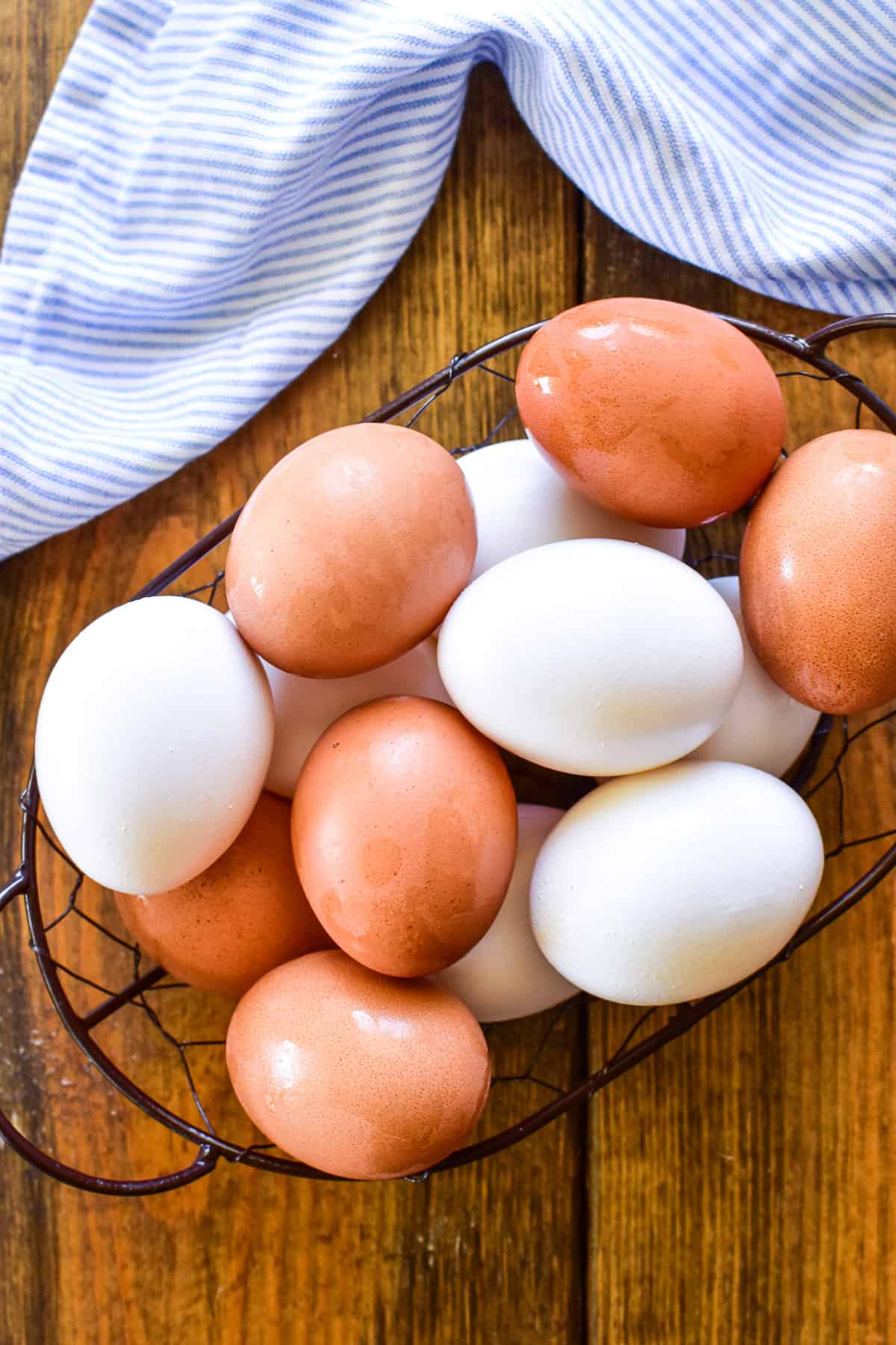 White and brown eggs in a wire basket with a blue and white striped napkin