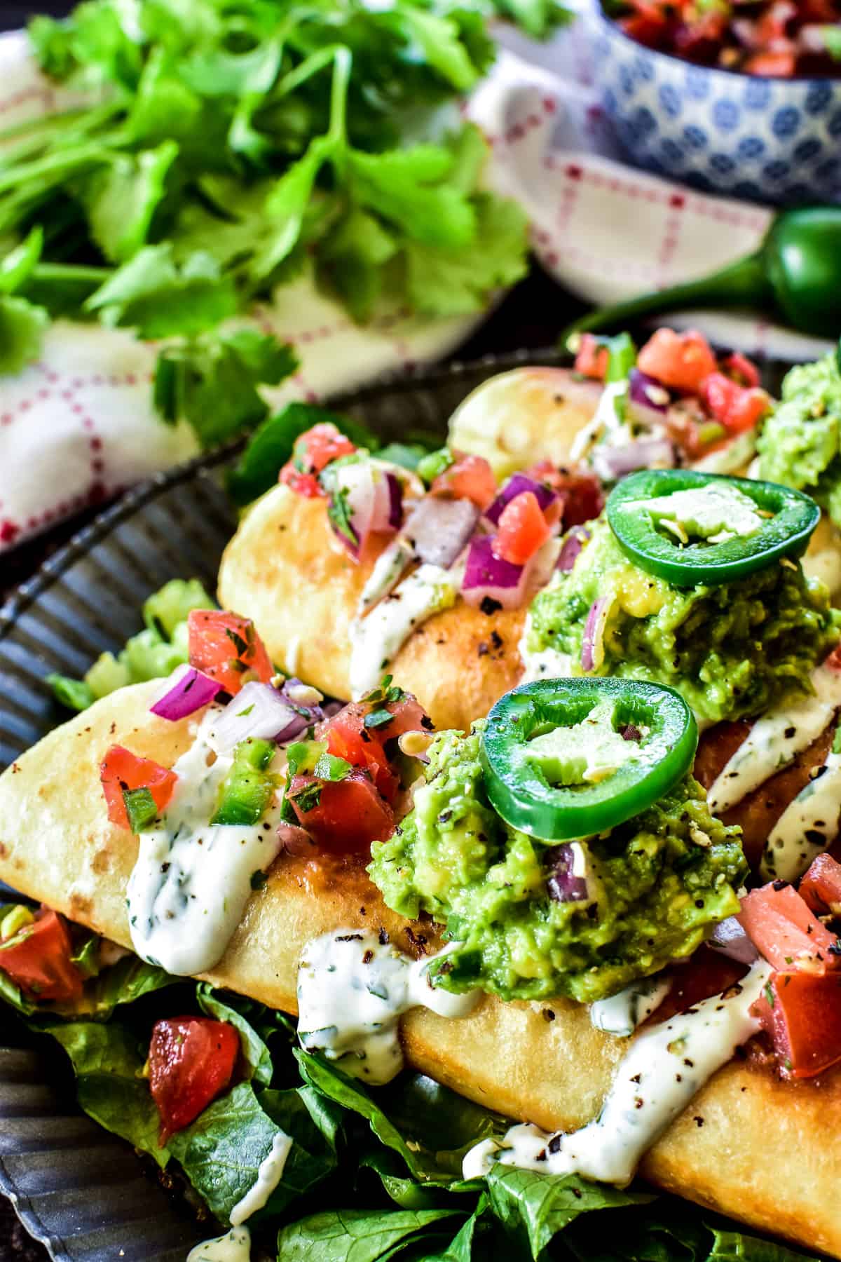 Close up of Creamy Chicken Flautas topped with pico de gallo, guacamole, and cilantro lime sauce