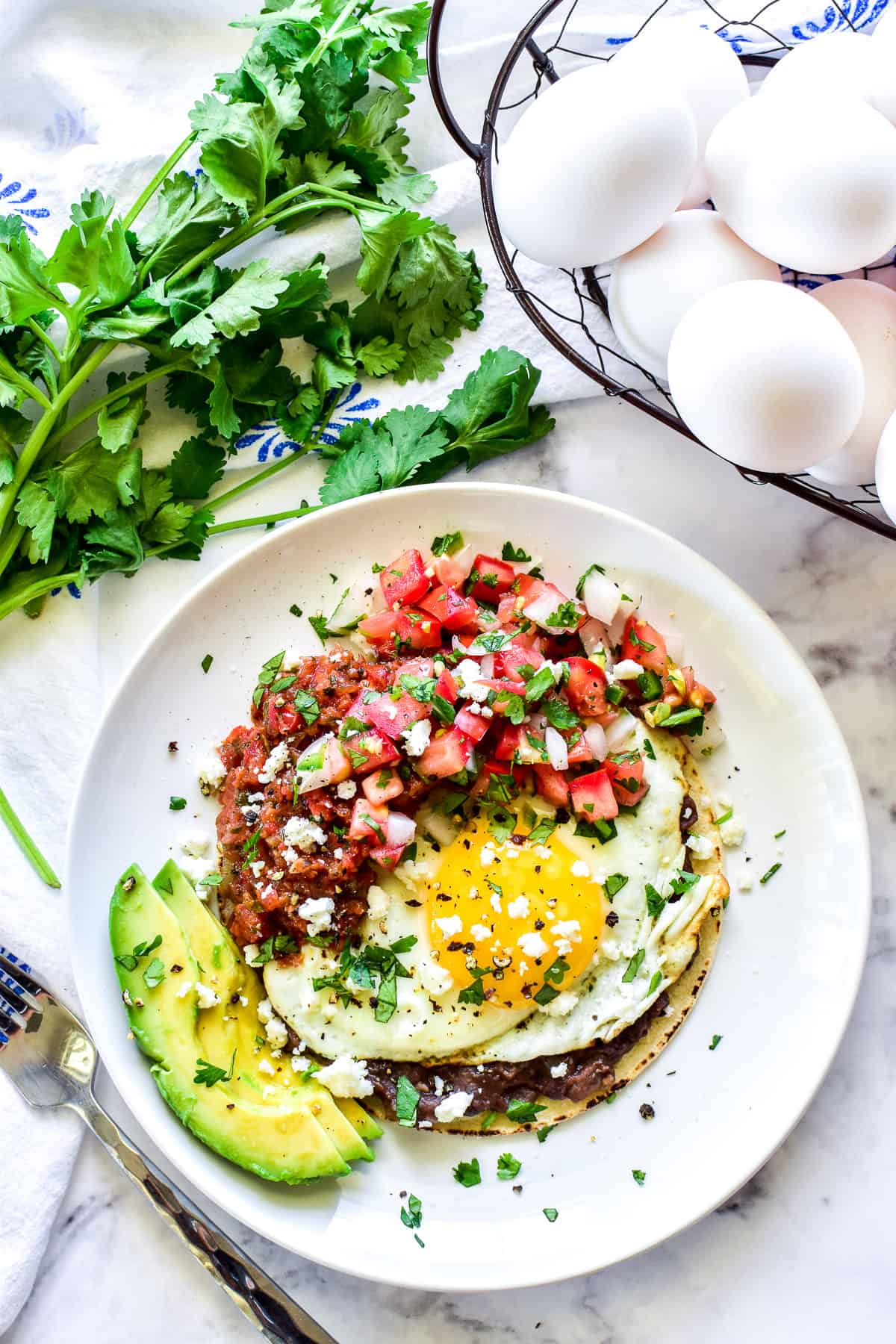 Overhead shot of Huevos Rancheros with a basket of eggs and fresh cilantro