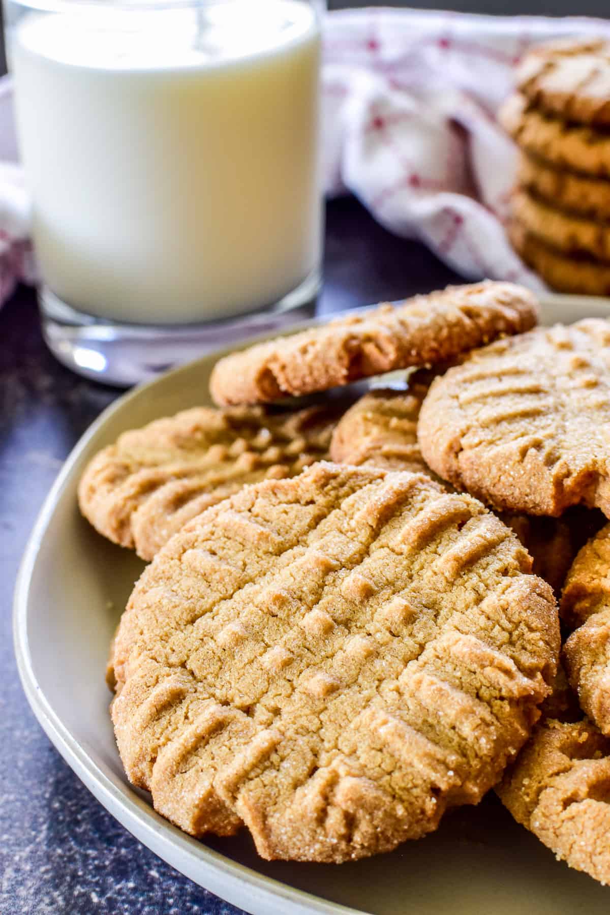 Side view of peanut butter cookies on a plate with a glass of milk