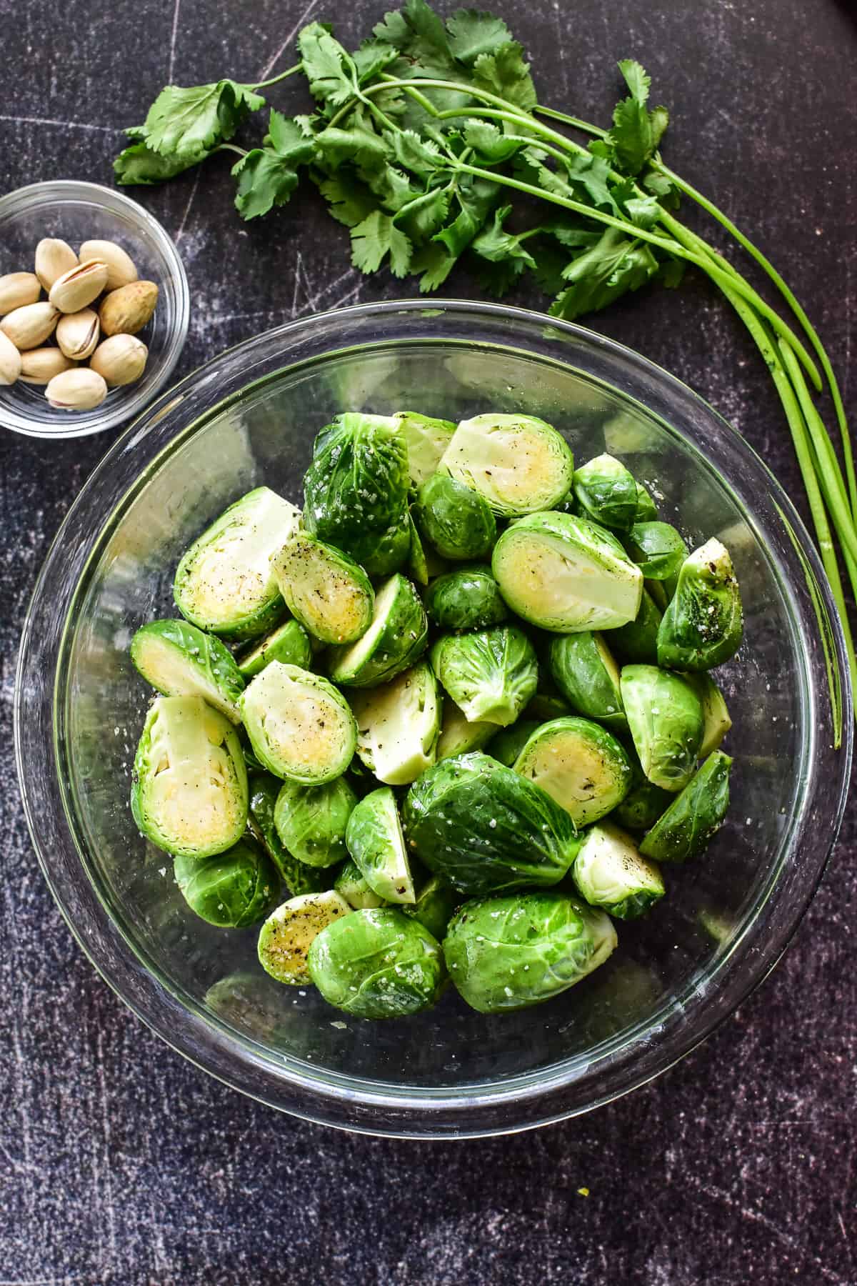 Brussels Sprouts cut in half in a glass bowl with seasonings