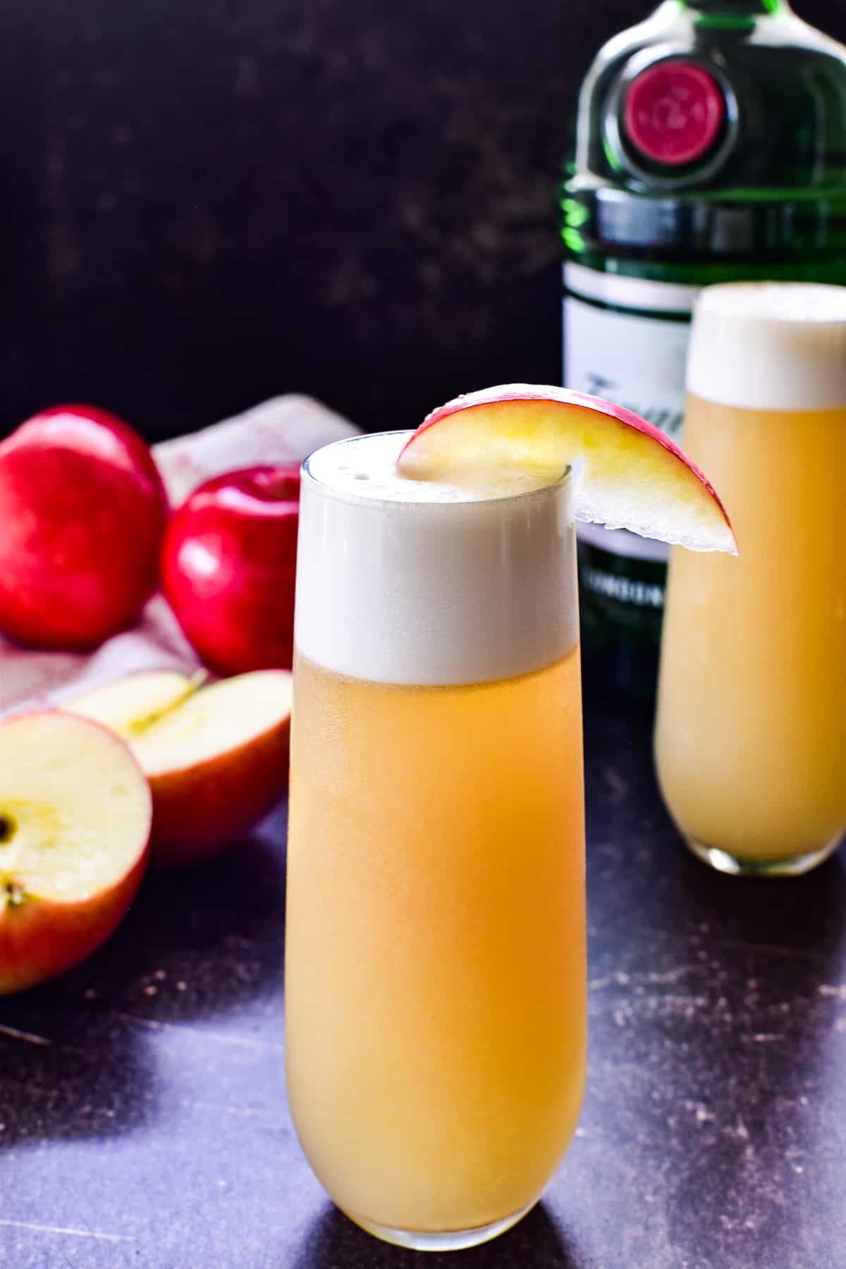 Apple Gin Fizz in a glass with a bottle of Tanqueray and fresh red apples