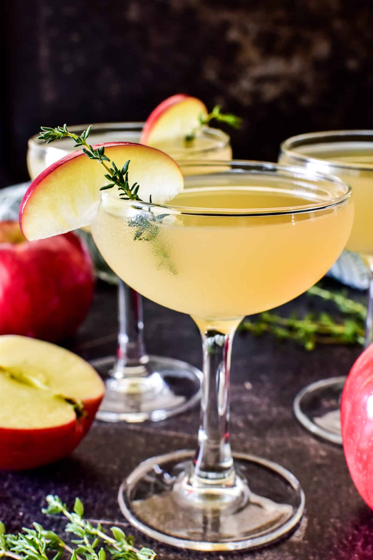 Close up of Appletini in a coupe glass garnished with apple and thyme