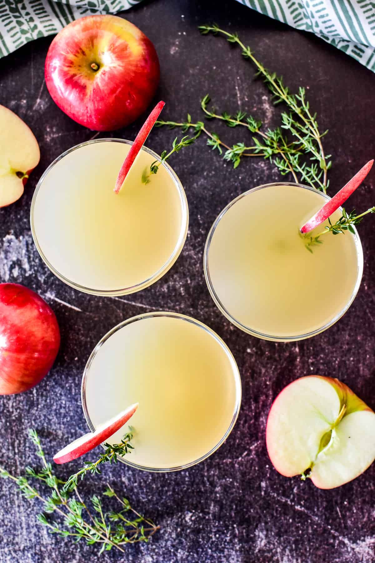 Overhead shot of 3 appletinis with fresh apples and thyme in the background