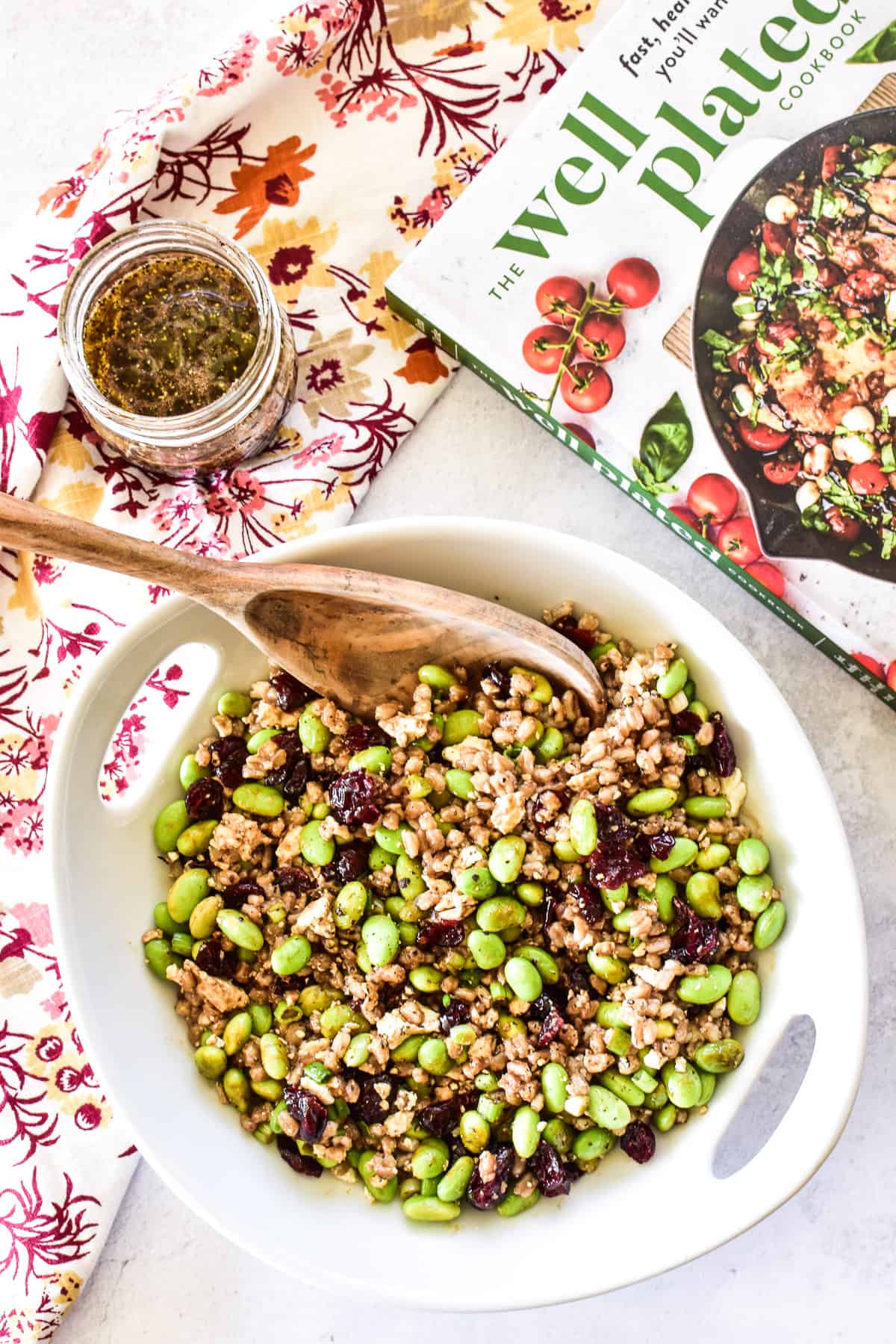 Overhead shot of Farro Salad in white serving bowl with The Well Plated Cookbook