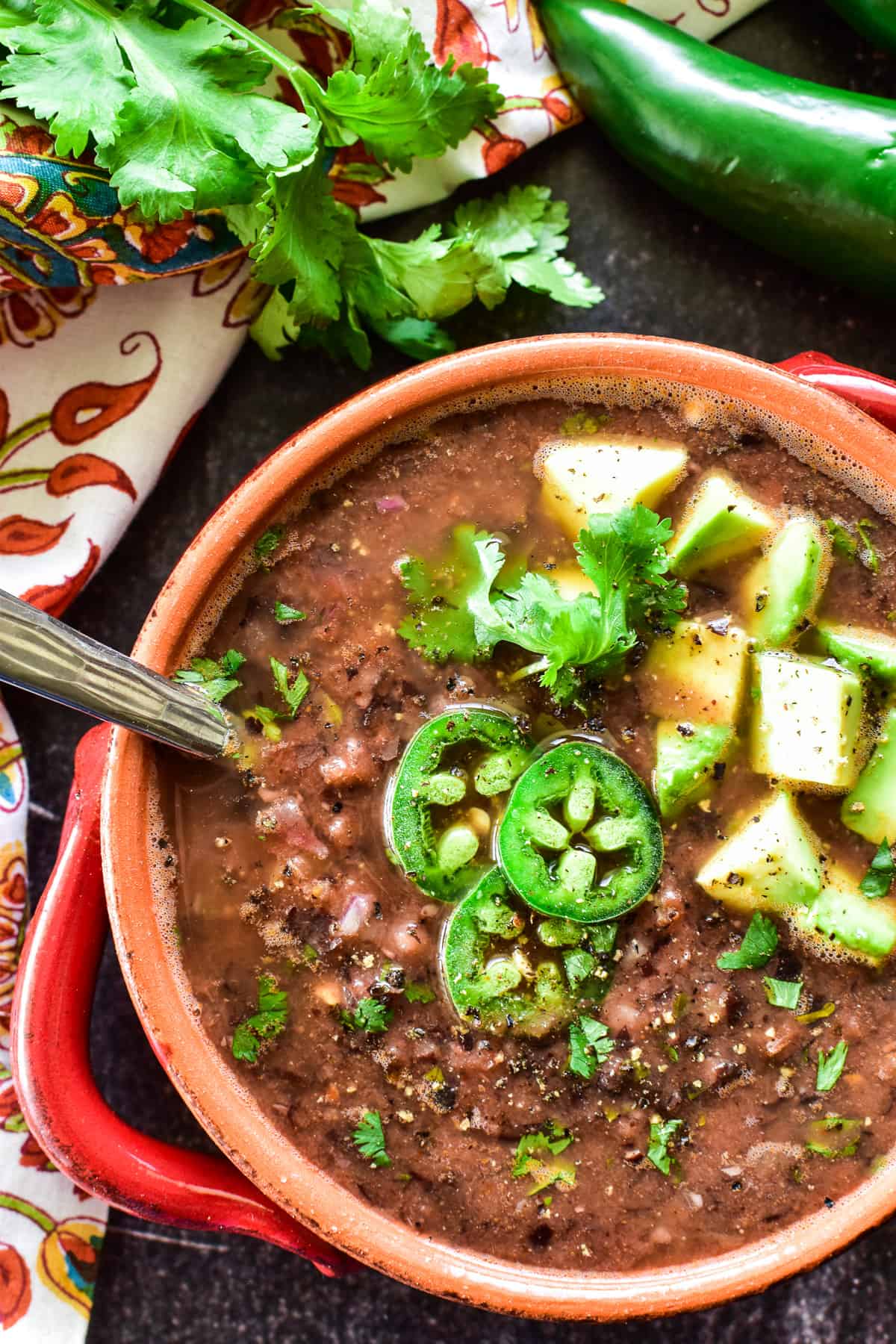 Overhead shot of Black Bean Soup in a red & orange bowl with fresh jalapenos and avocado