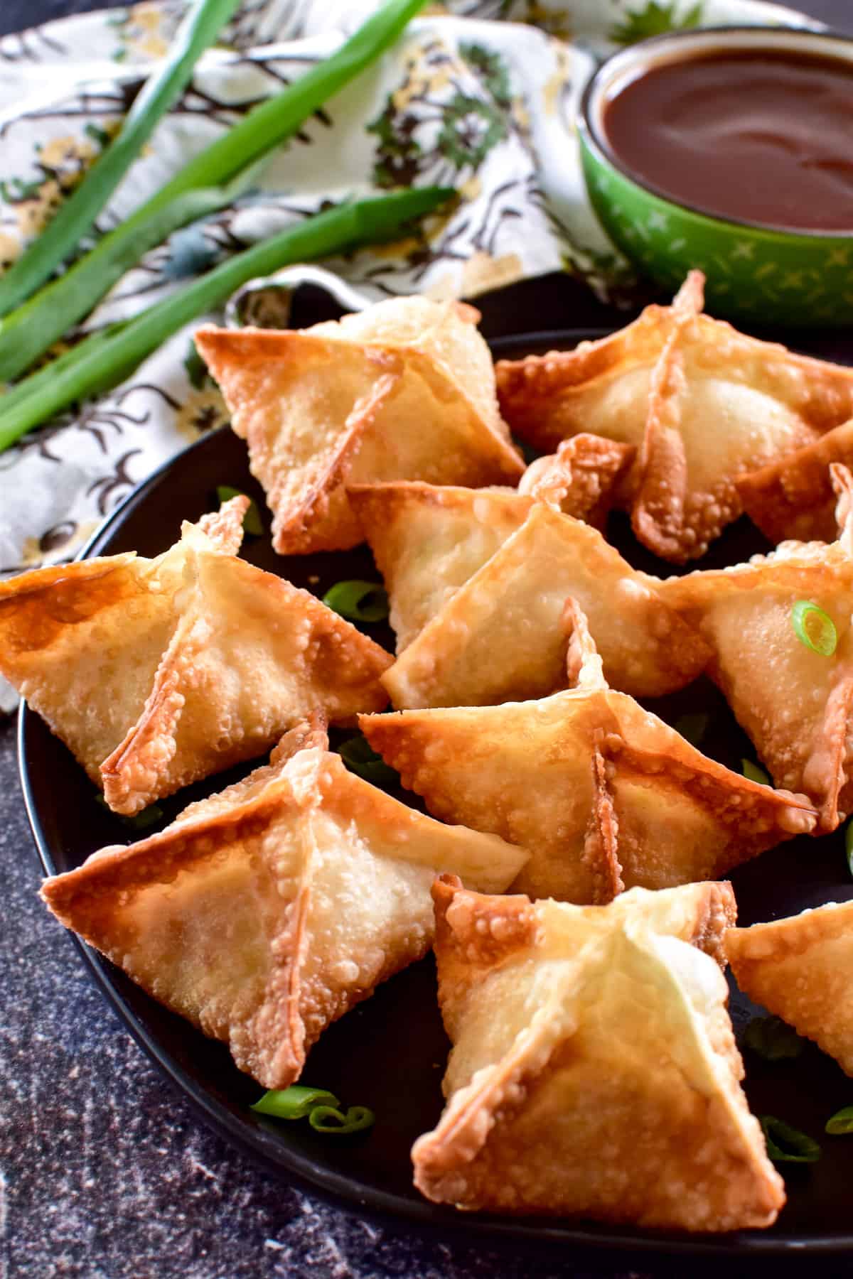 Side view of Crab Rangoon with green onions and sweet & sour sauce