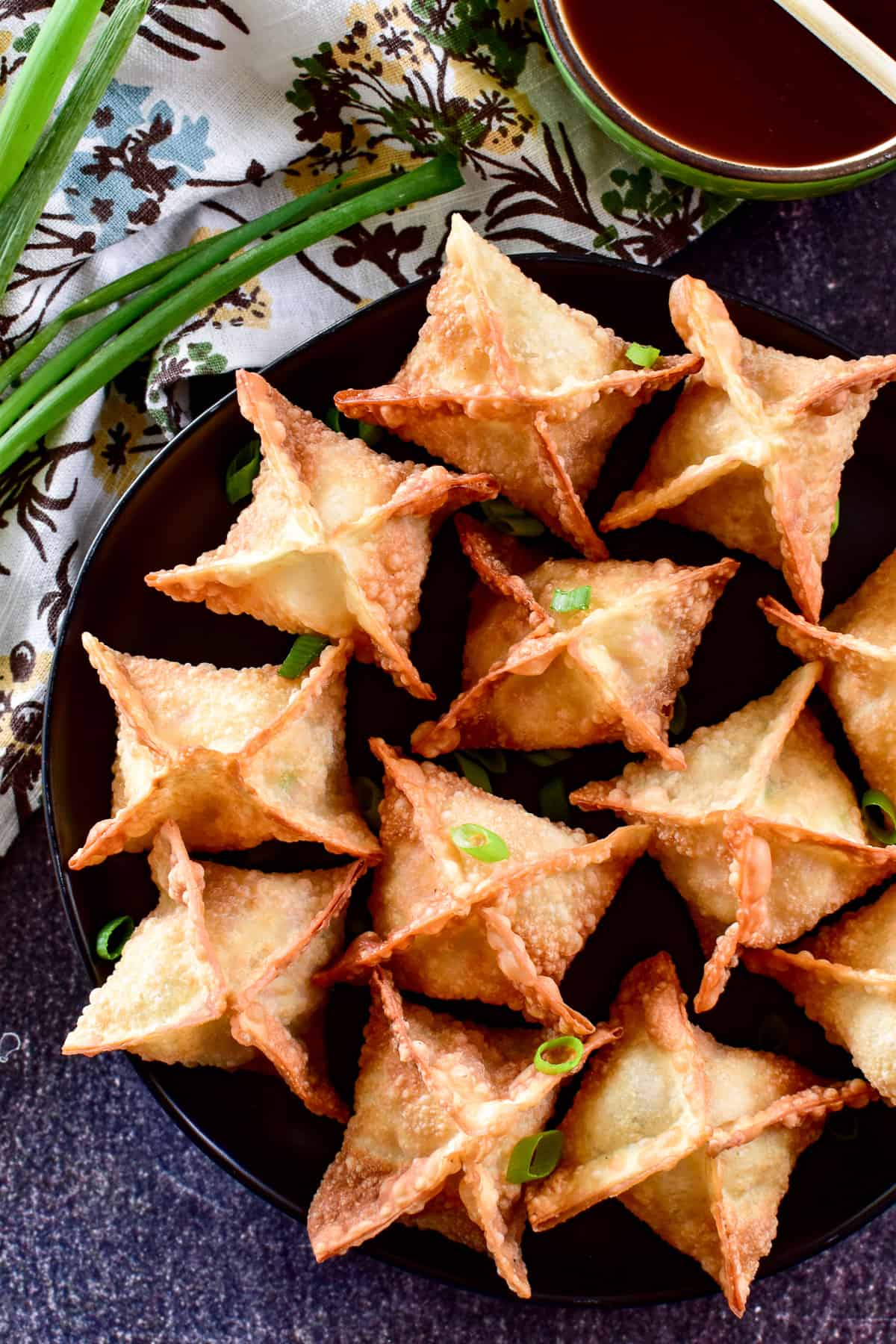 Overhead shot of Crab Rangoon on a black plate with sweet & sour sauce