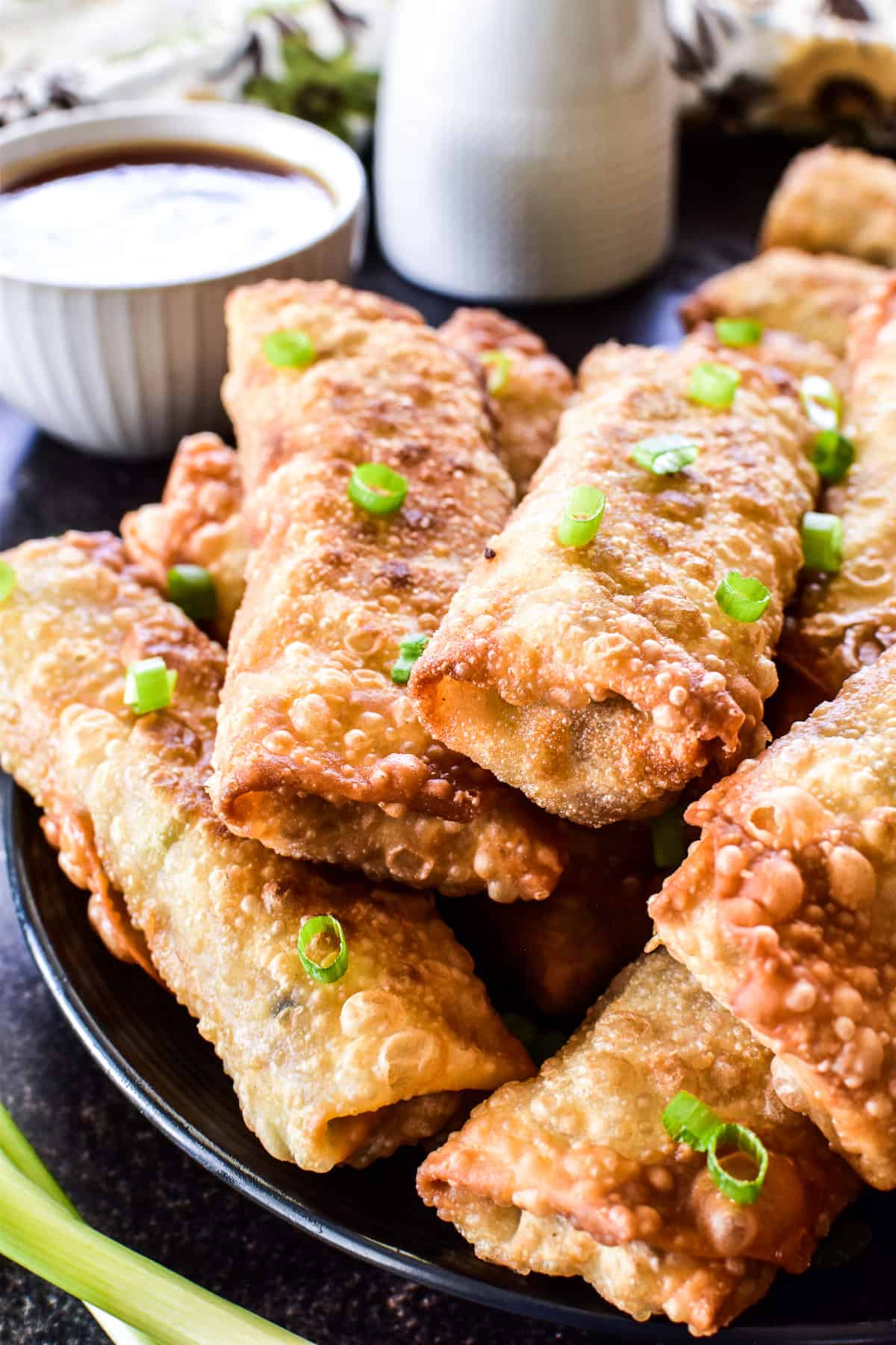 Close up of egg rolls on a black plate with green onion garnish