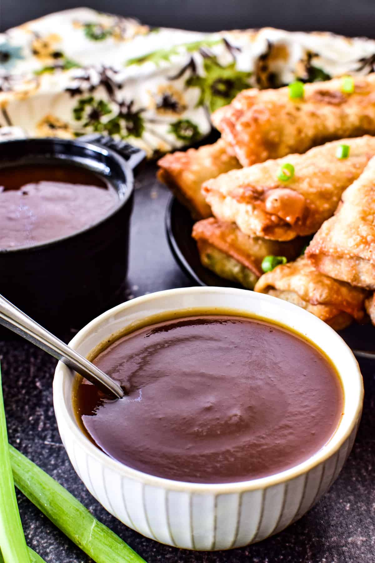 Close up of sweet and sour sauce with egg rolls in the background