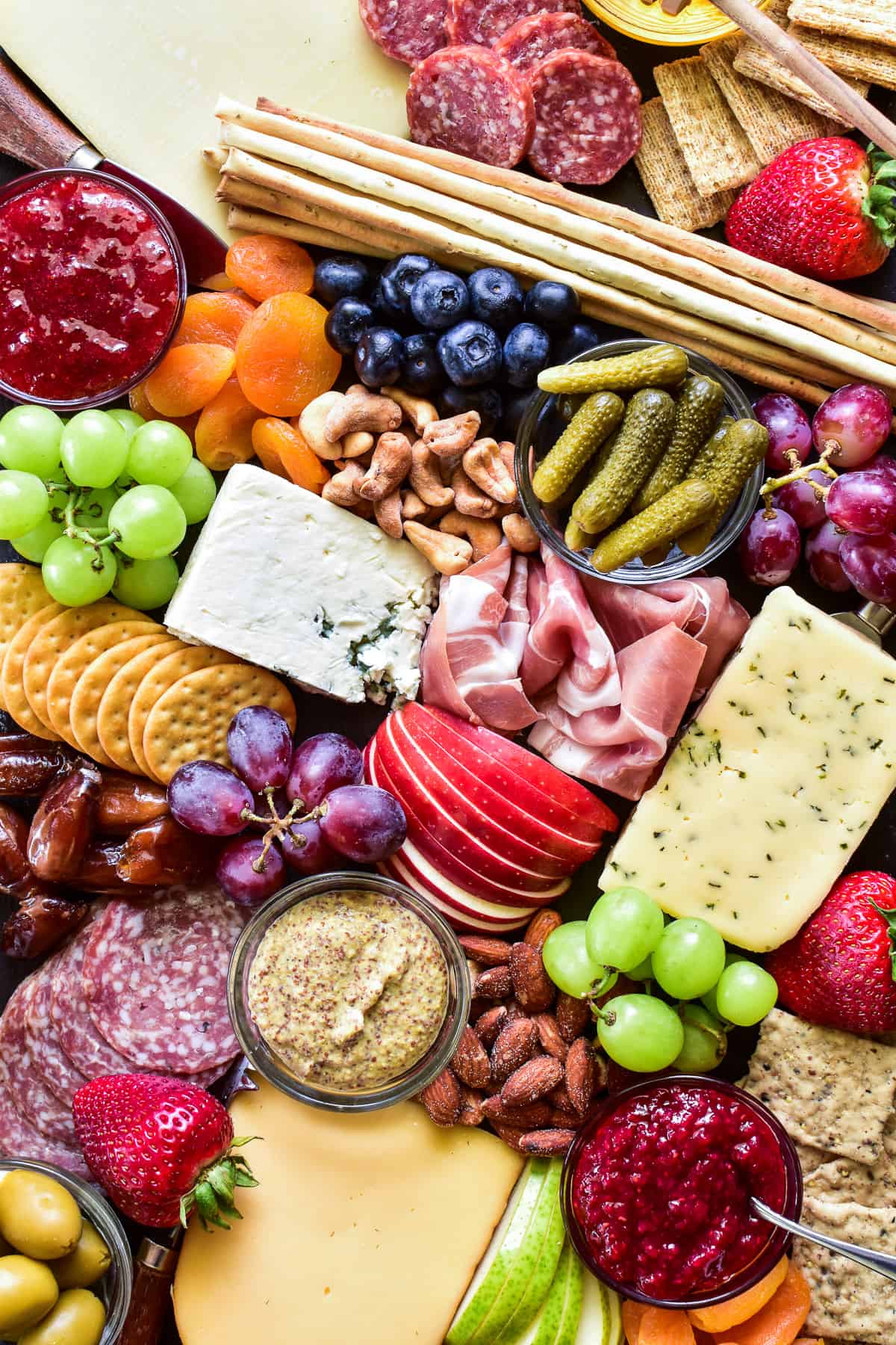 Overhead shot of meats, cheeses, crackers, fruits, nuts, and condiments on a charcuterie board