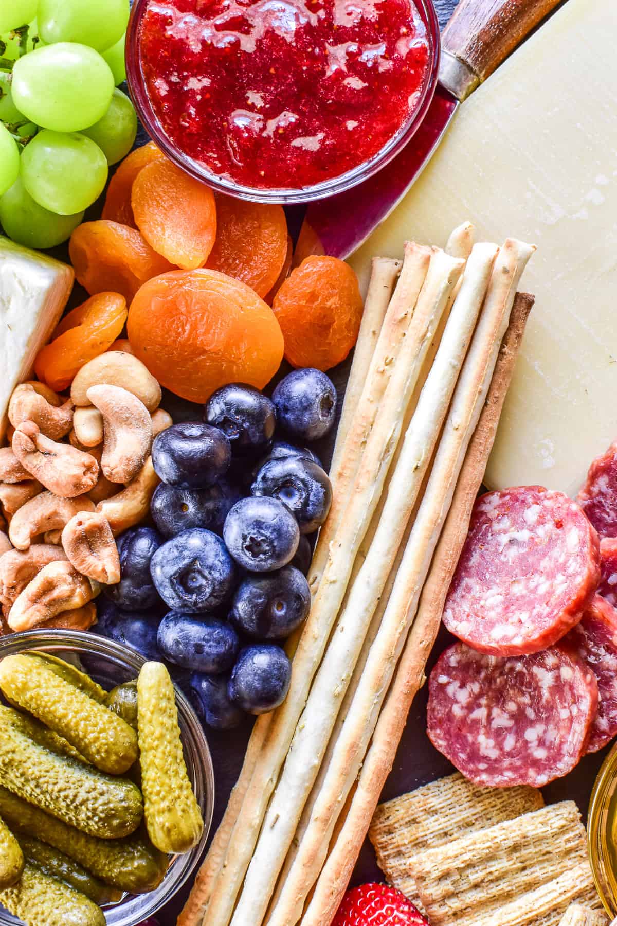 Close up of blueberries, dried apricots, cashews, cheese, salami, and breadsticks