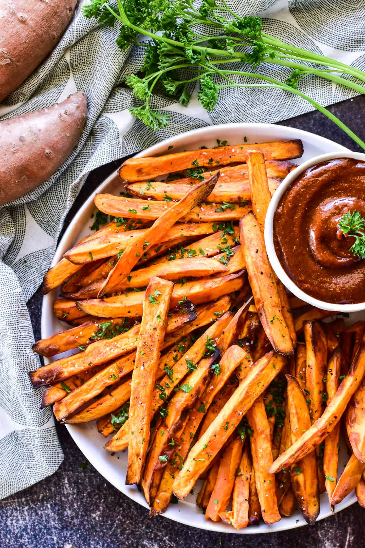 Overhead shot of Sweet Potato Fries on a white plate with fresh parsley and curry ketchup