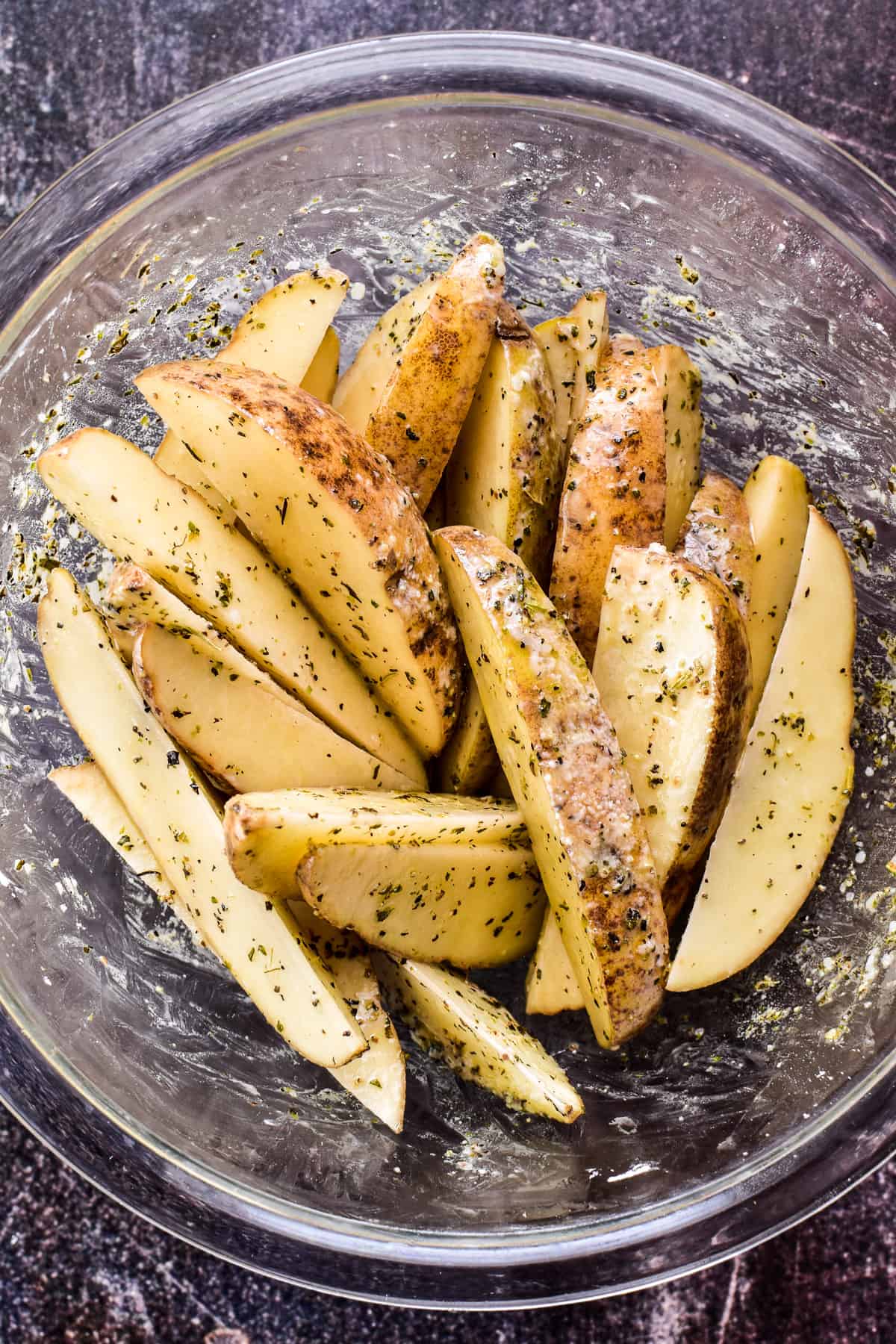 Potato Wedges combined with oil, seasonings, and cornstarch in a glass mixing bowl