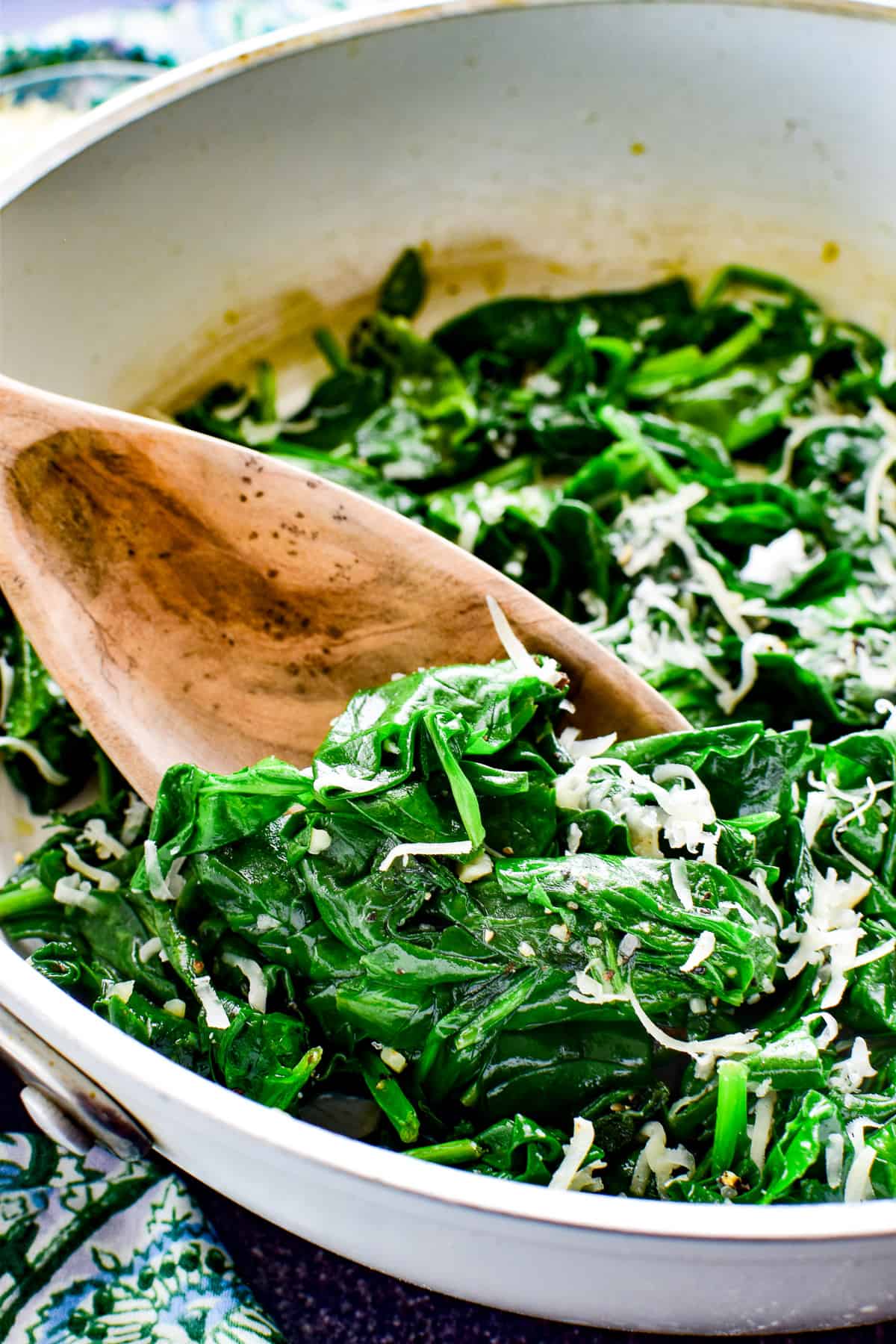 Sauteed Spinach in white skillet with a wooden spoon
