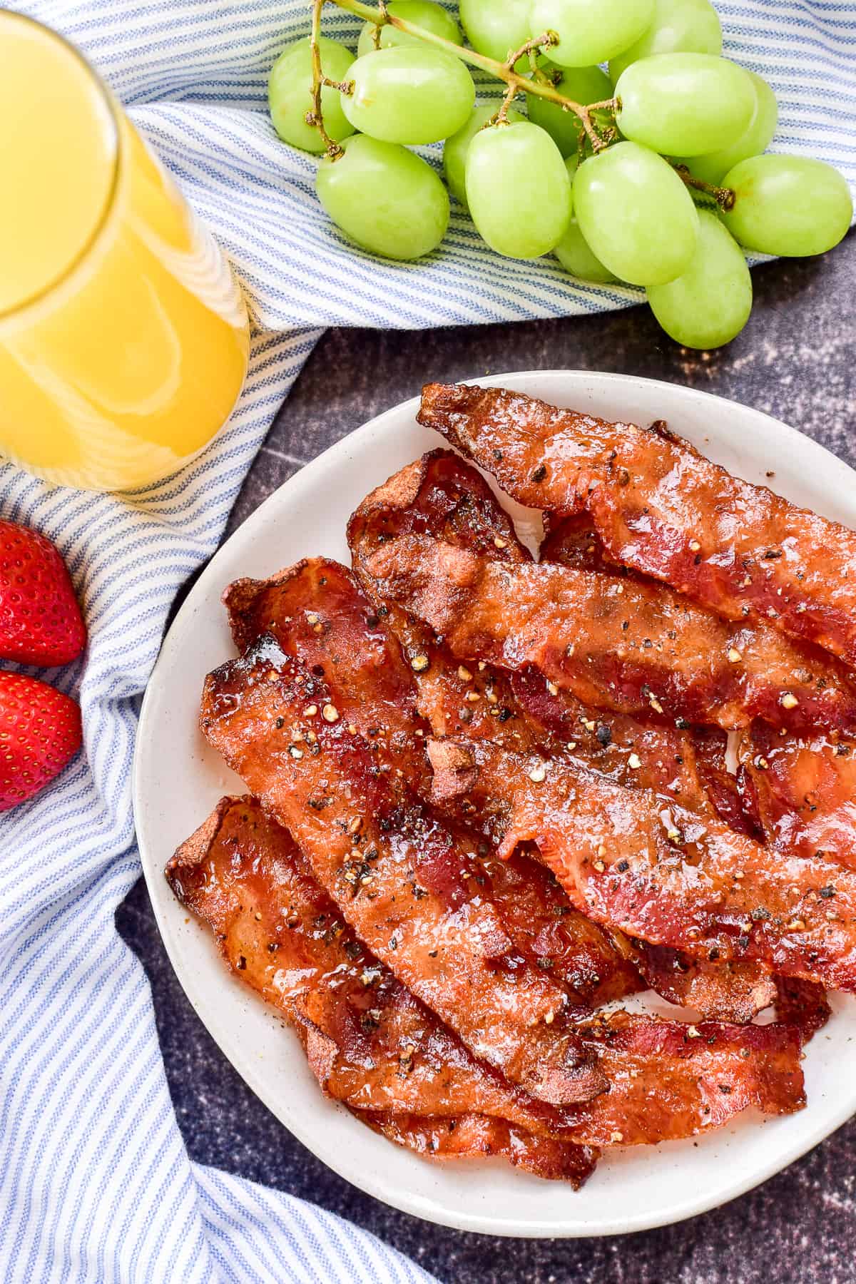 Candied Bacon on a white plate with fruit & orange juice