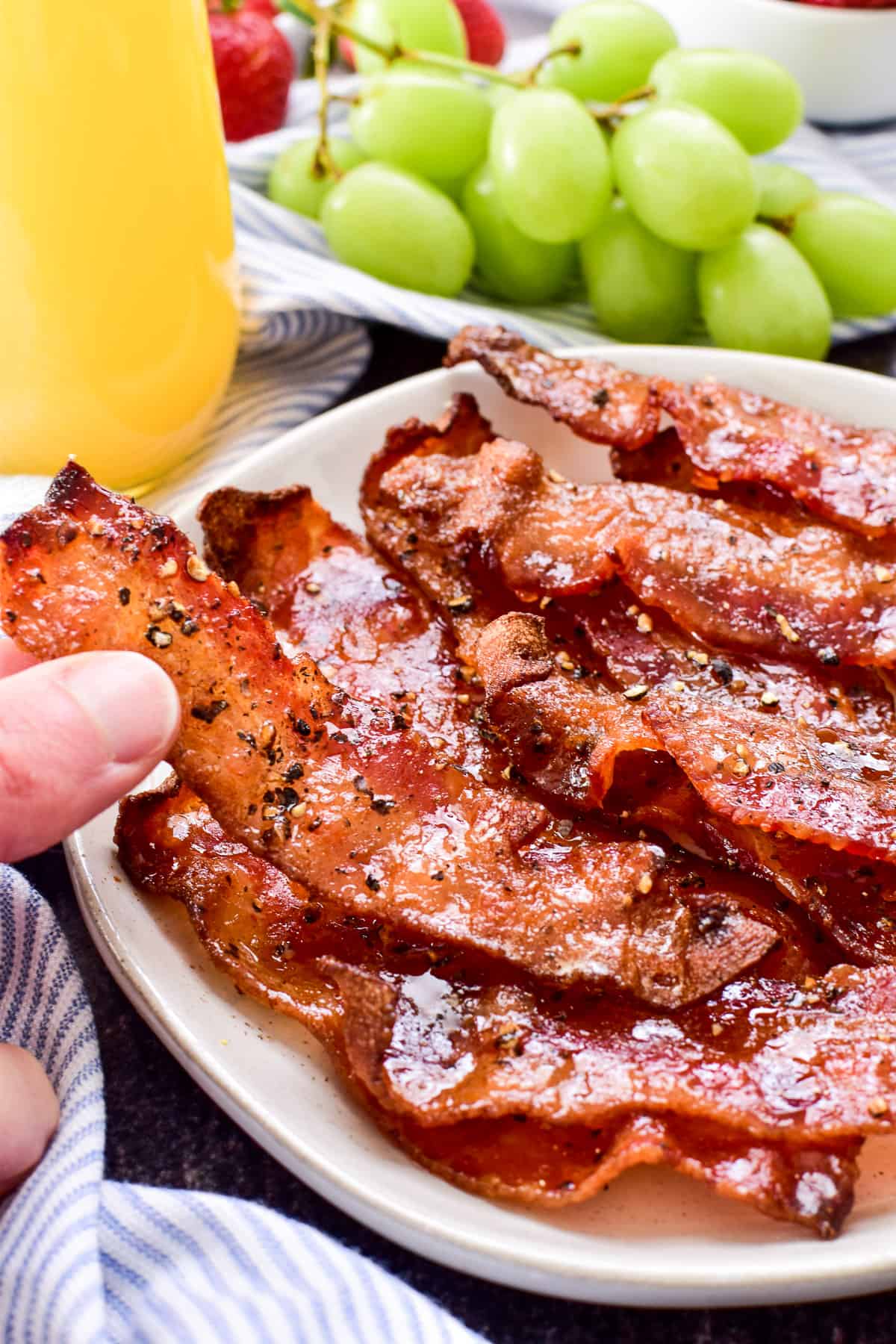 Hand grabbing Candied Bacon from a white plate