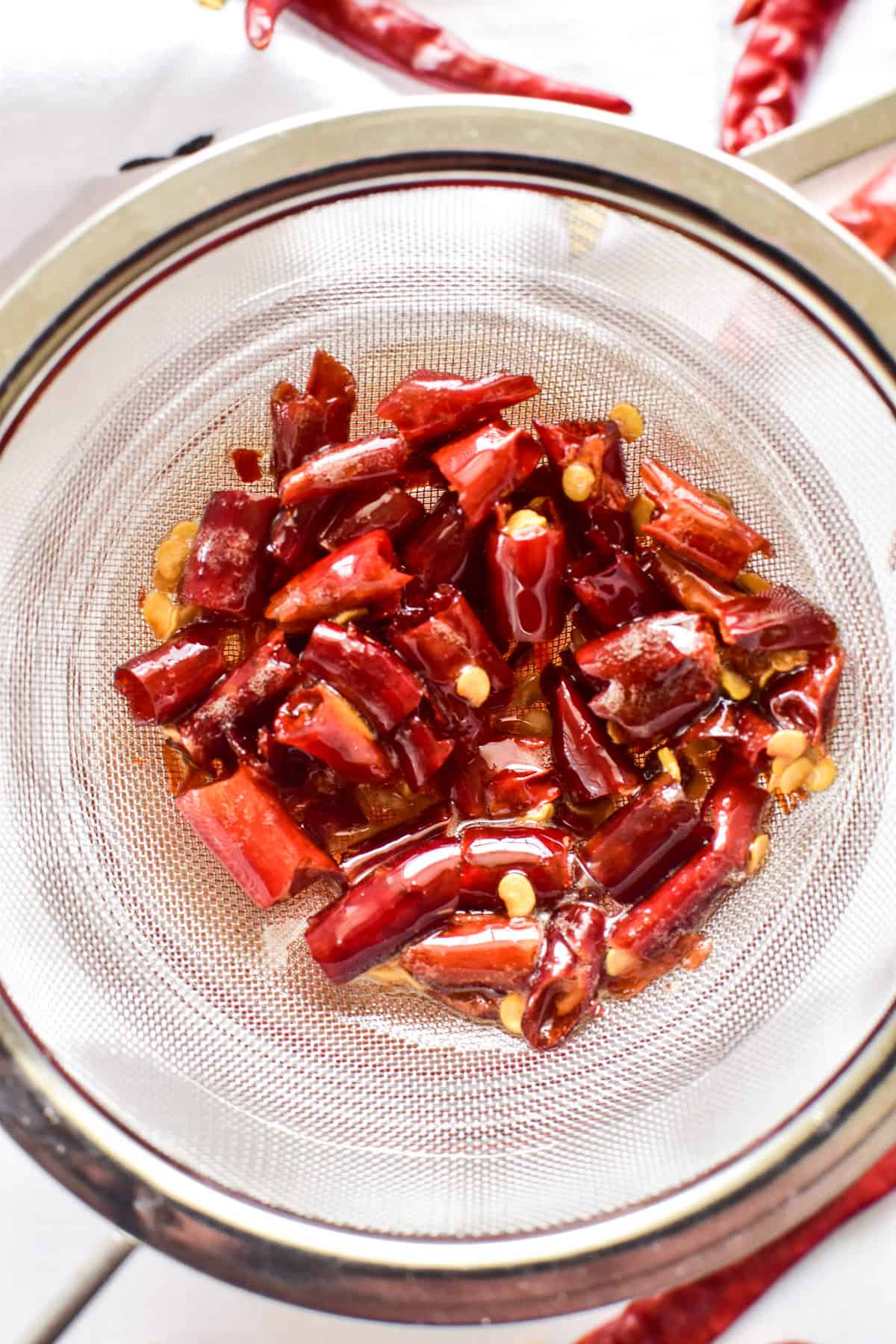 Overhead image of chopped chili peppers being strained from hot honey