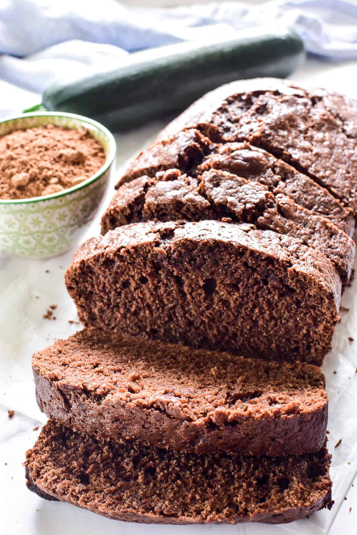 Chocolate Zucchini Bread sliced with cocoa powder and fresh zucchini