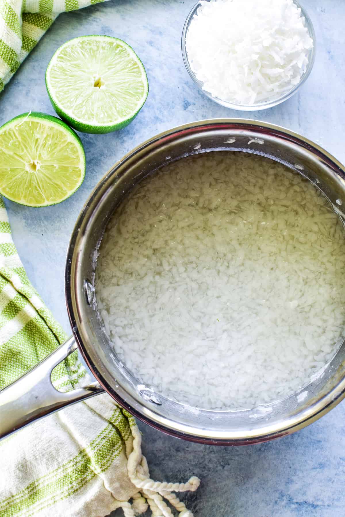 Coconut Lime Simple Syrup in a saucepan with limes and shredded coconut