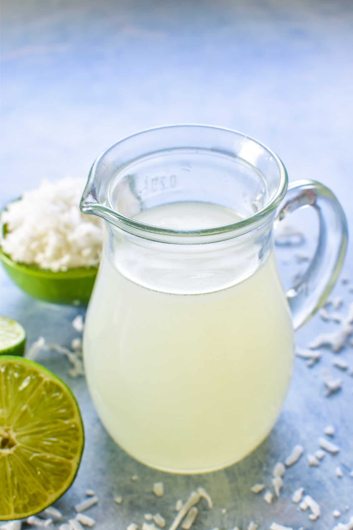 Coconut Lime Simple Syrup in a small pitcher with shredded coconut in a green bowl