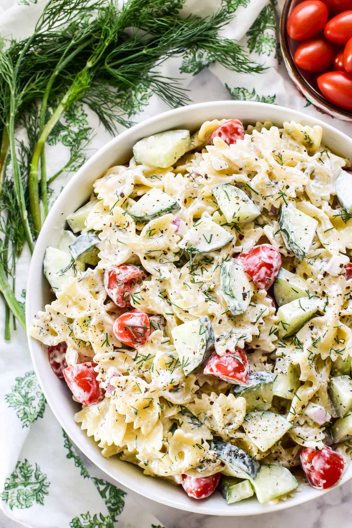 Overhead image of Cucumber Pasta Salad in a white bowl with fresh dill and tomatoes