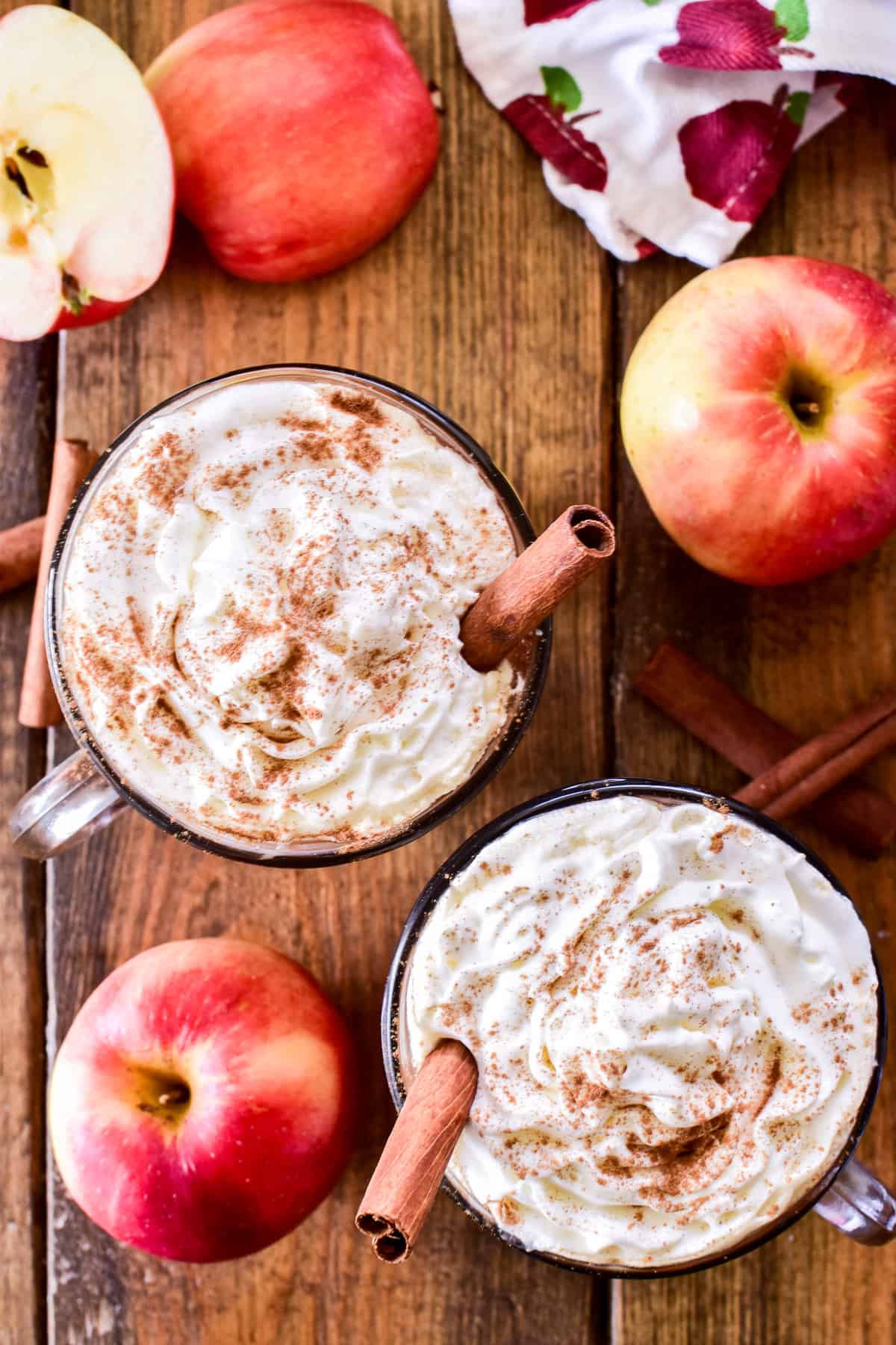 Overhead image of two mugs of Spiked Apple Cider with fresh apples and cinnamon sticks