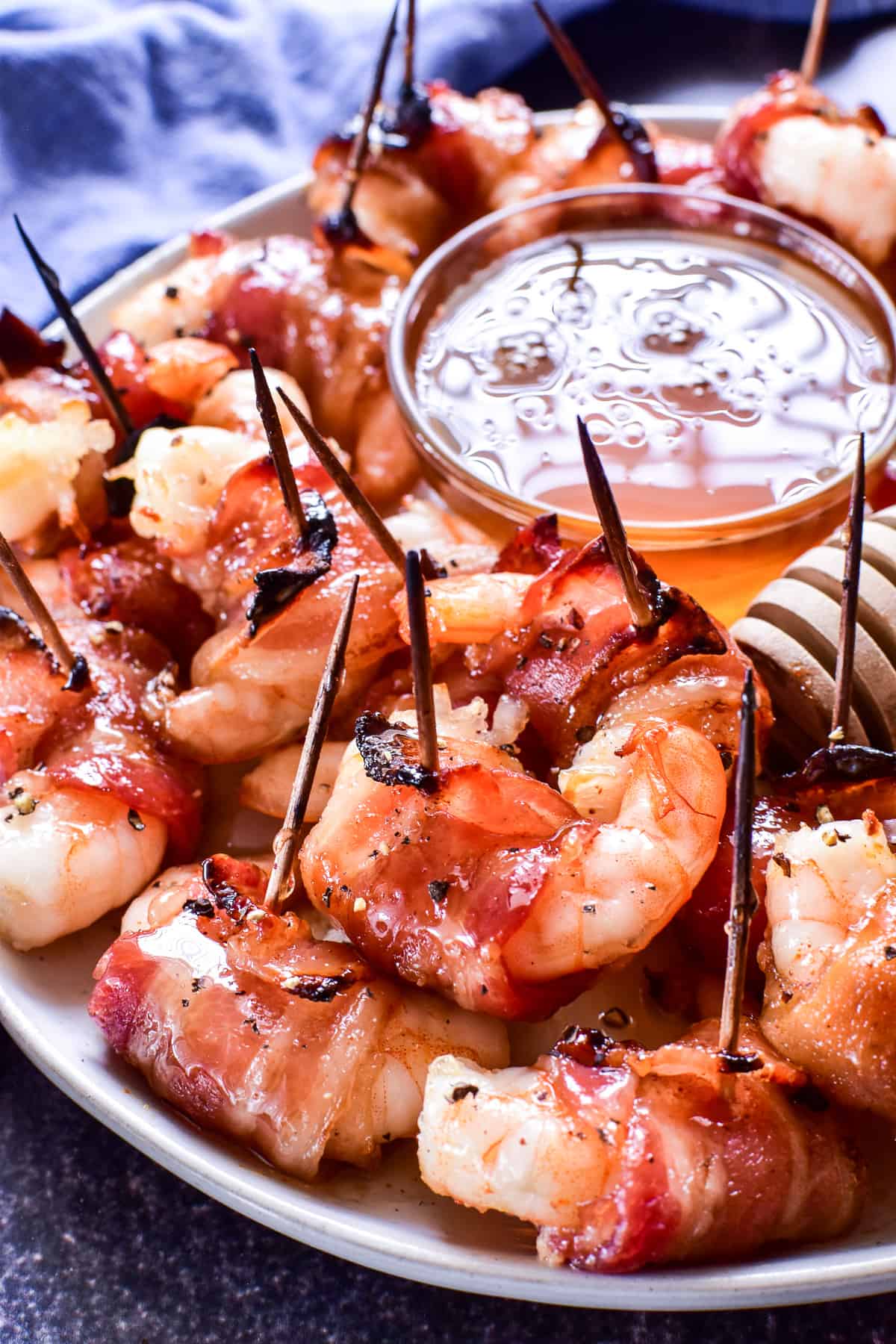 Bacon wrapped shrimp on a white plate with honey 