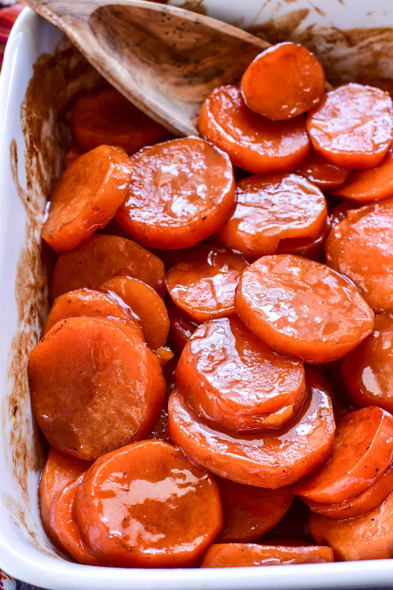 Closeup of Candied Yams in a white baking dish with a wooden spoon