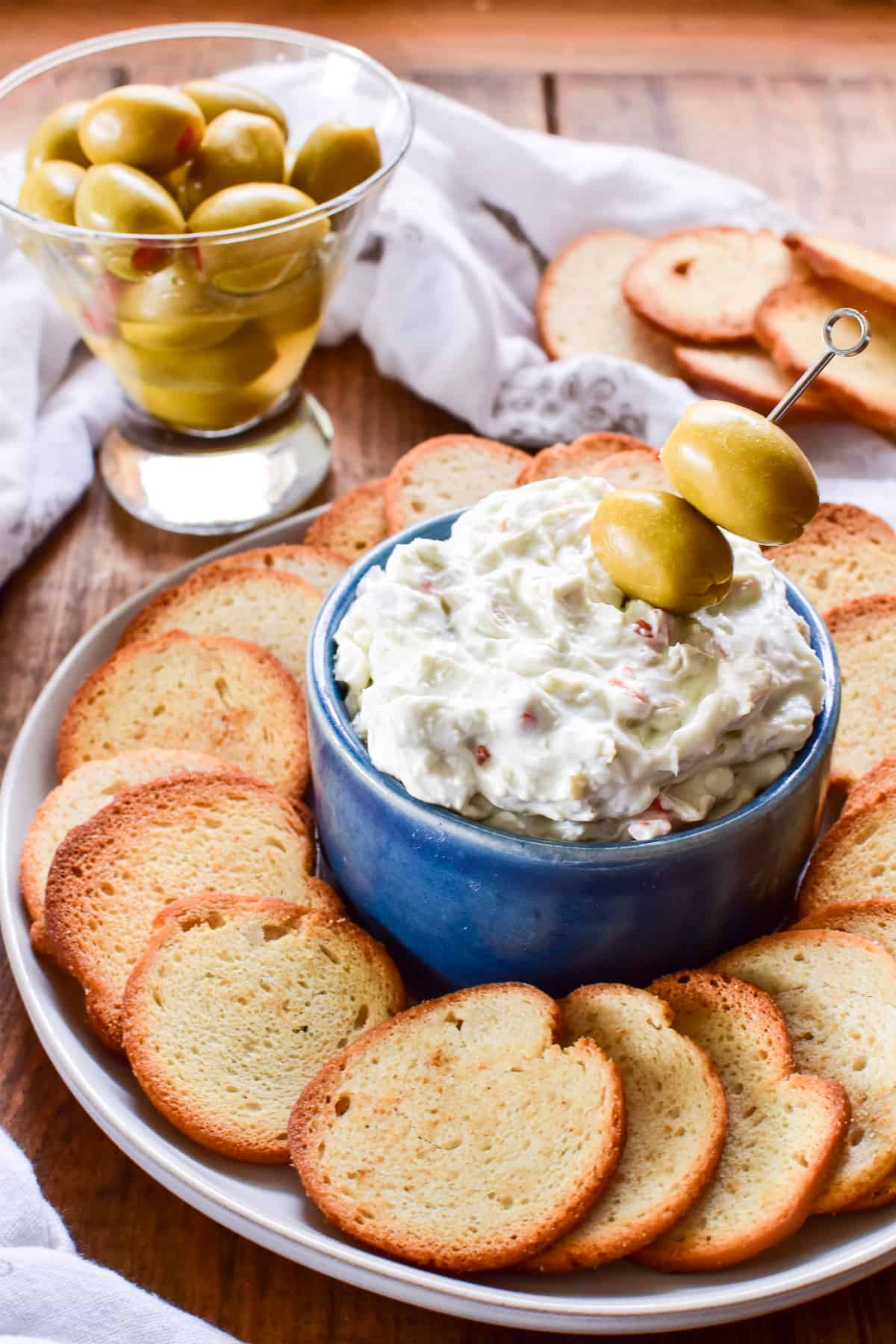 Dirty Martini Dip with bagel chips and olives on a white plate