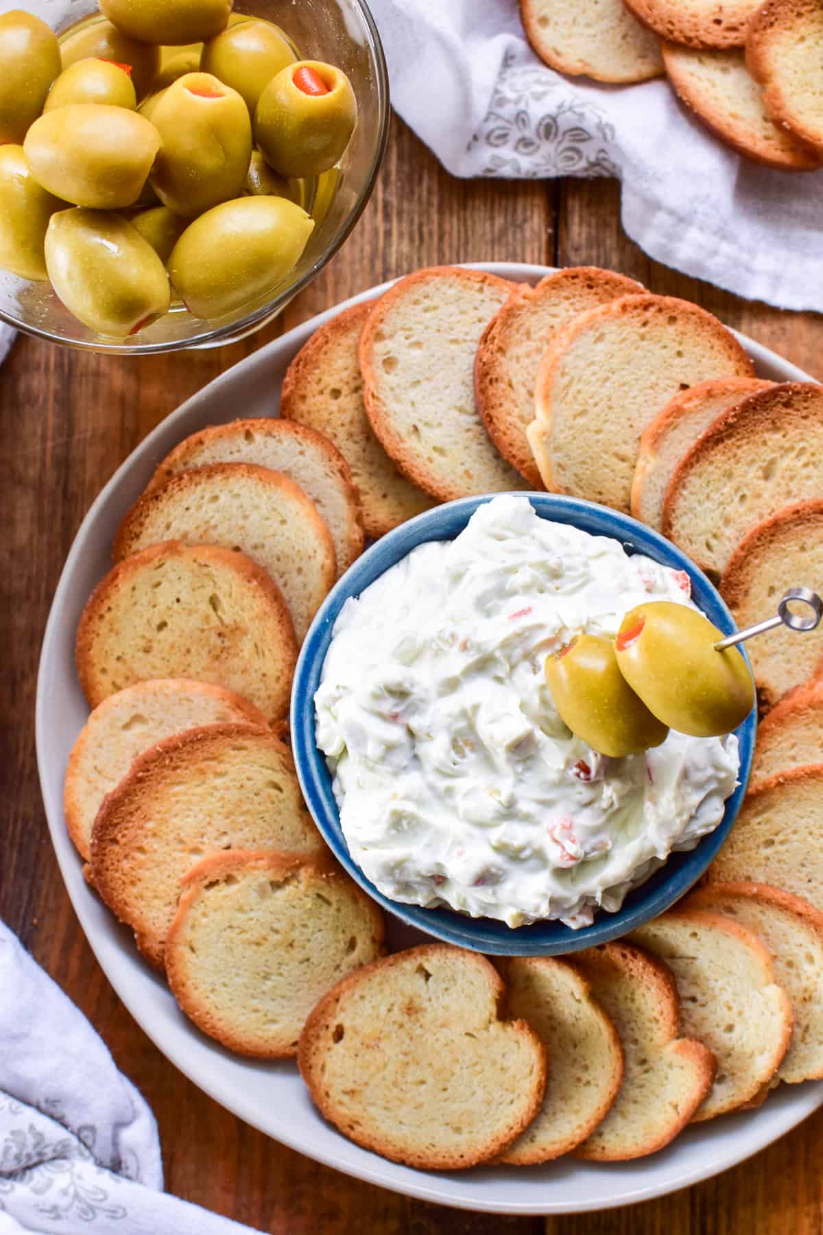 Overhead image of Dirty Martini Dip surrounded by bagel chips and a martini glass filled with olives