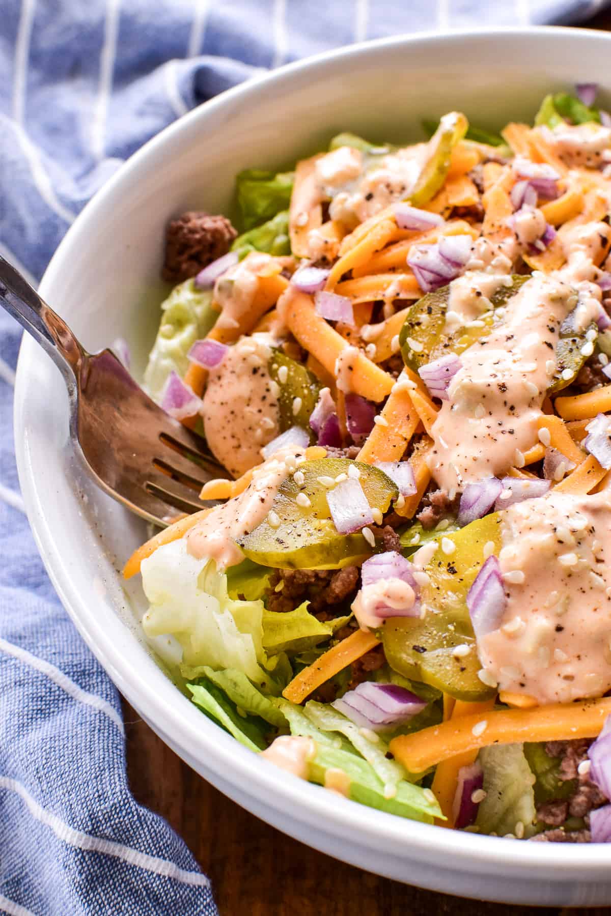 Big Mac Salad in a white bowl with a blue and white striped towel