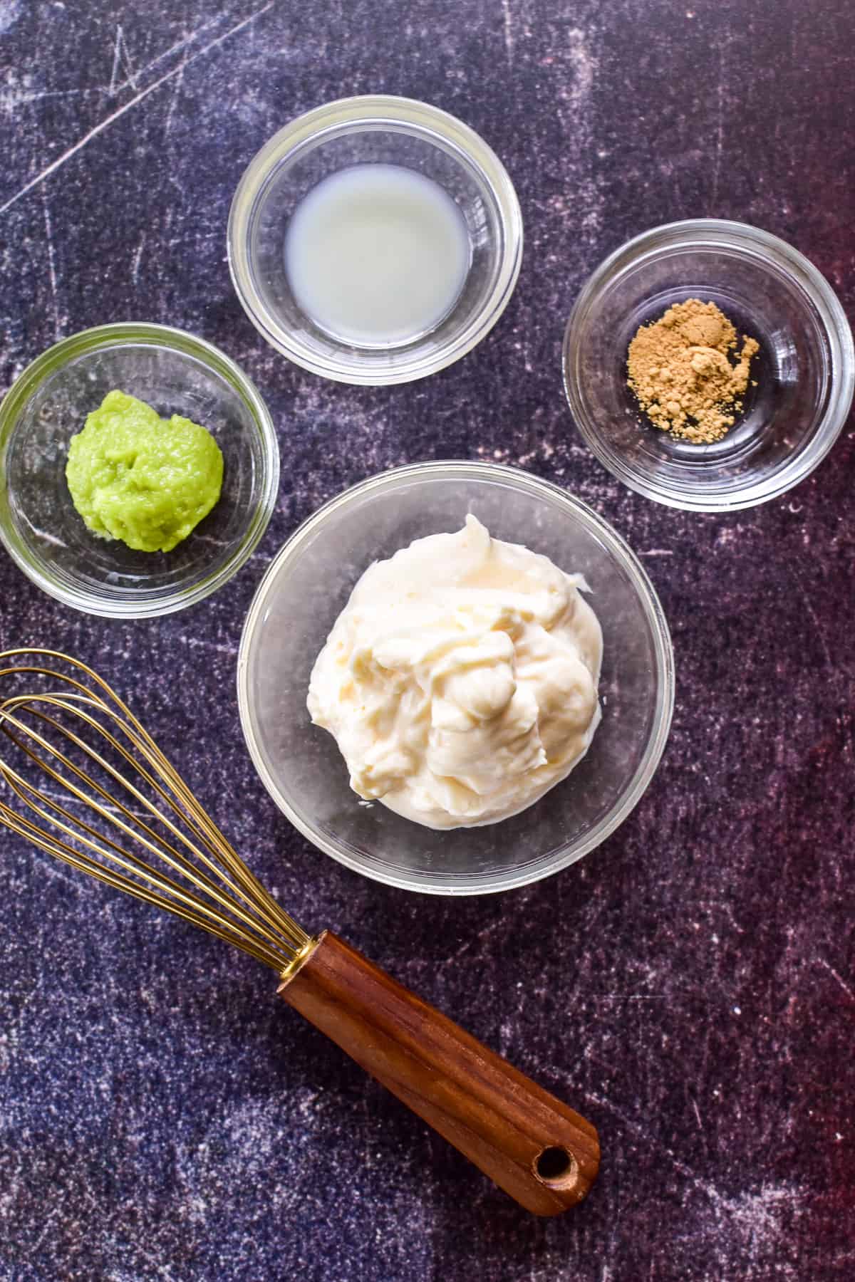 Wasabi Mayo ingredients in clear glass mixing bowls with a gold and wood handled whisk