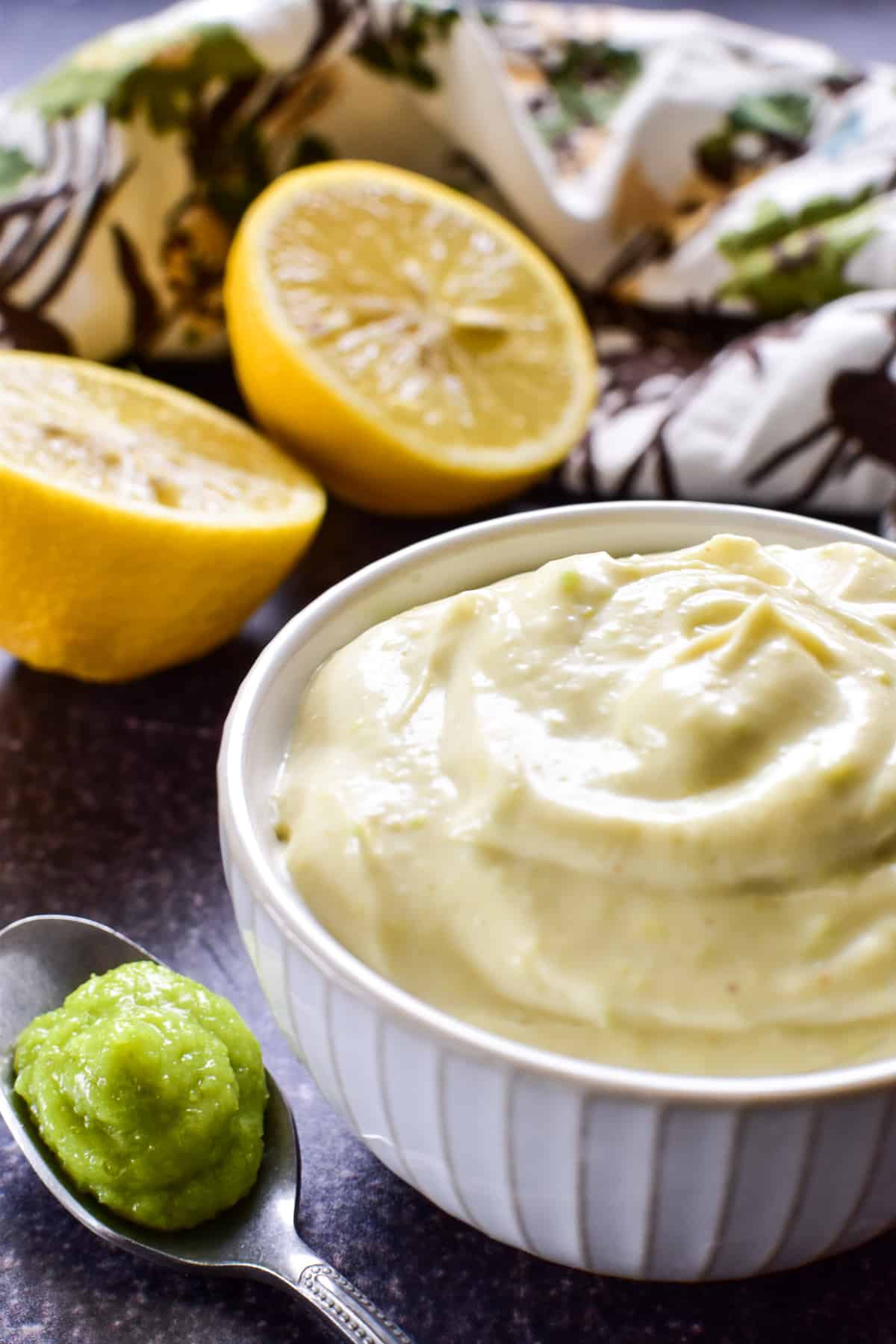Side view of Wasabi Mayo in a small white bowl with a spoonful of wasabi paste and a cut lemon